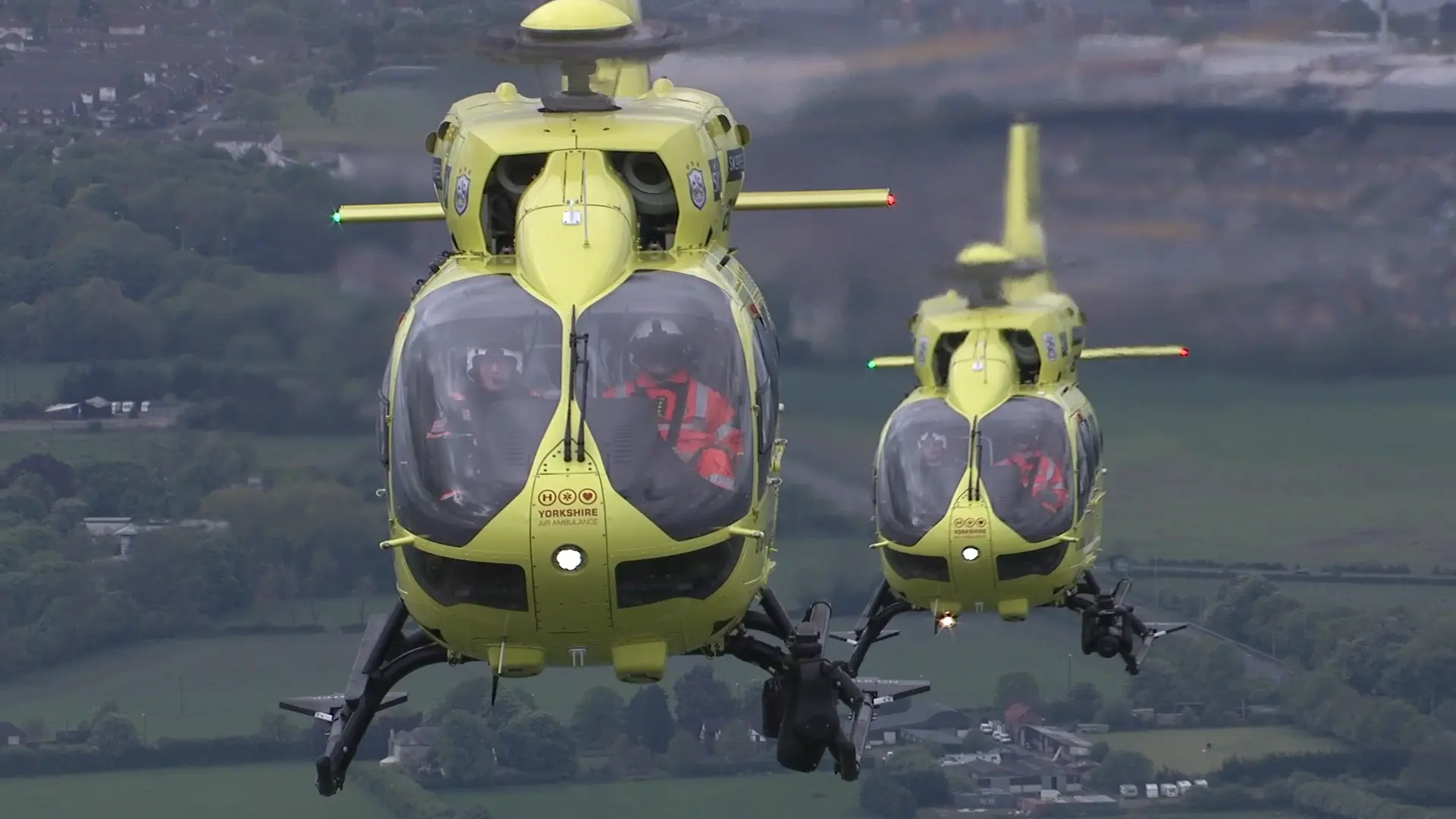 Two Yorkshire Air Ambulance helicopters flying side by side over rural Yorkshire.