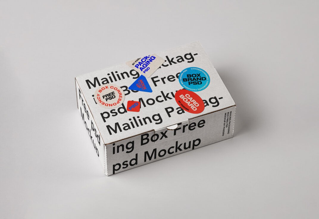 Mailing box mockup featuring a white cardboard box with bold black text wrapping its surface. Decorated with colorful circular and triangular stickers, displayed on a light gray background.