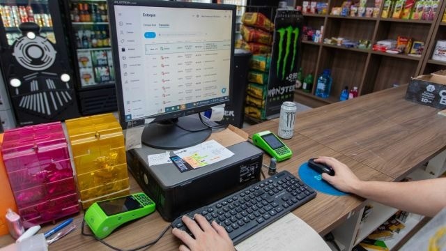 Tela do sistema de gestão Nex aberta na aba de controle de estoque em computador sobre balcão de vendas de uma loja de bebidas.