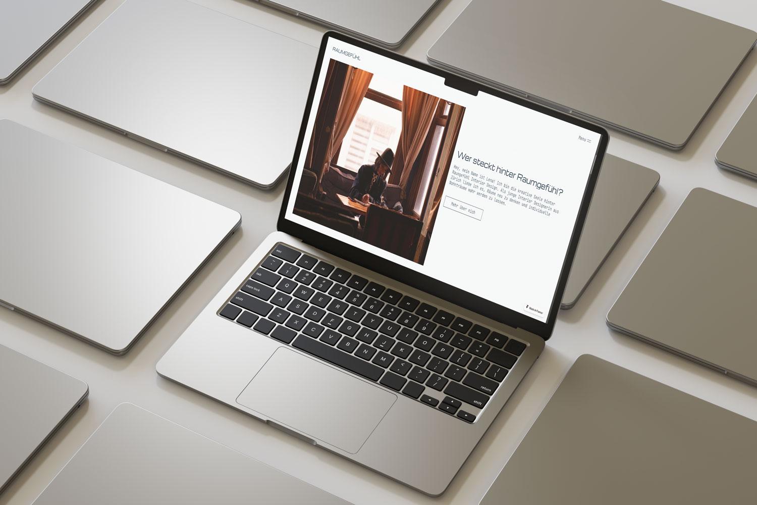 Mockup eines MacBooks inmitten mehrerer geschlossener Laptops. Auf dem Bildschirm ist die Raumgefühl-Website geöffnet, mit einem Bild einer Person am Schreibtisch und dem Text ‚Wer steckt hinter Raumgefühl?