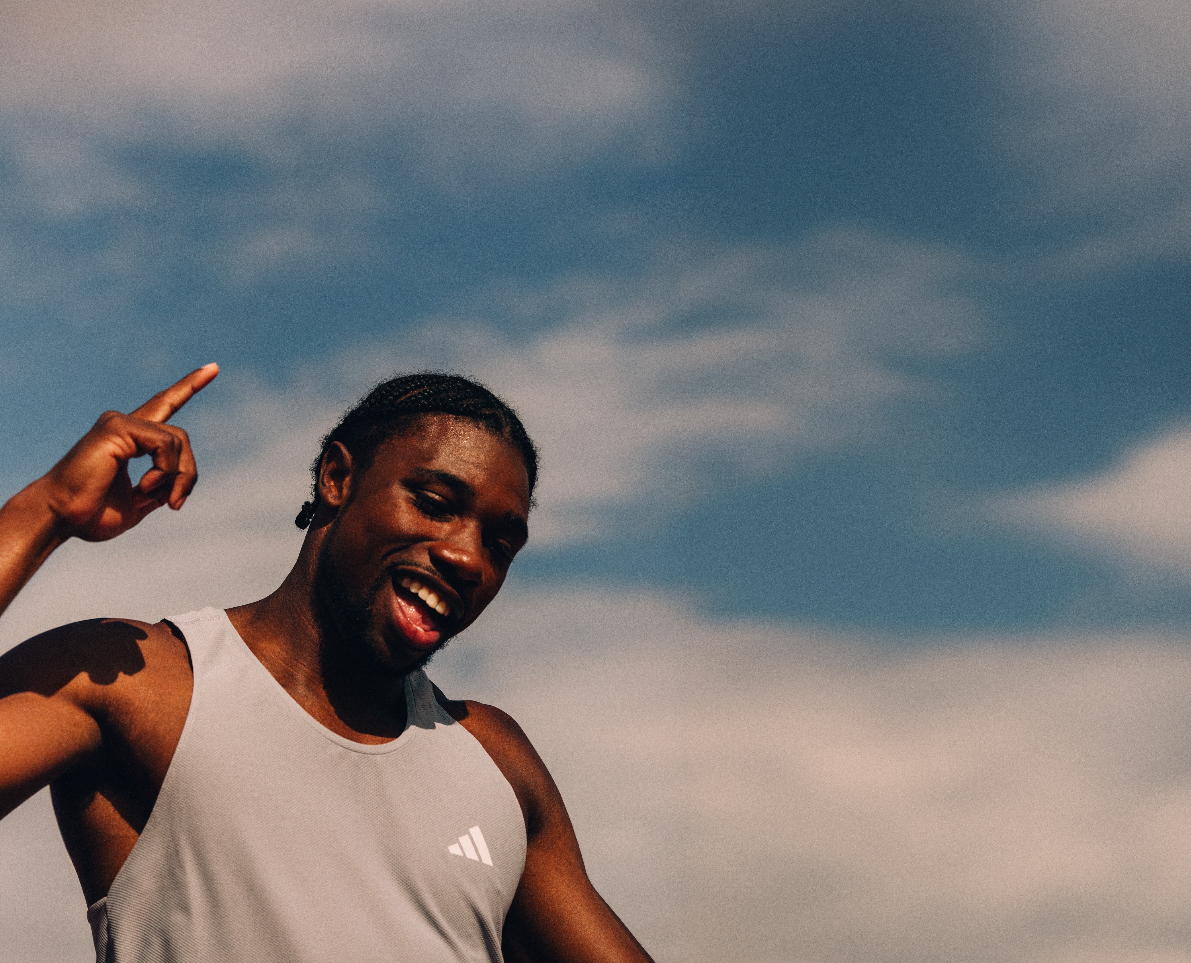 Inquadratura dal basso di Noah Lyles sorridente con sfondo cielo, studio della direzione artistica e prospettiva fotografica.
