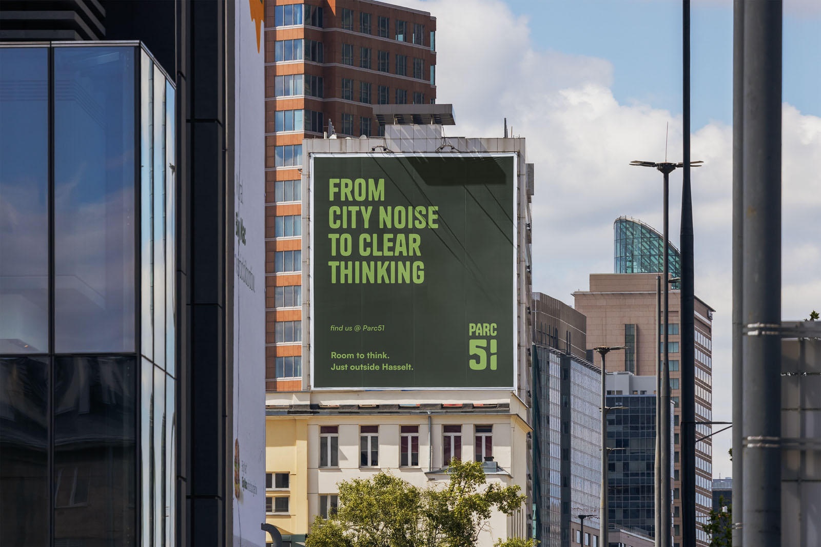 Een groot groen billboard op de zijkant van een kantoorgebouw in een stedelijke omgeving. De tekst op de poster luidt: "FROM CITY NOISE TO CLEAR THINKING", met onderaan het logo van Parc51.