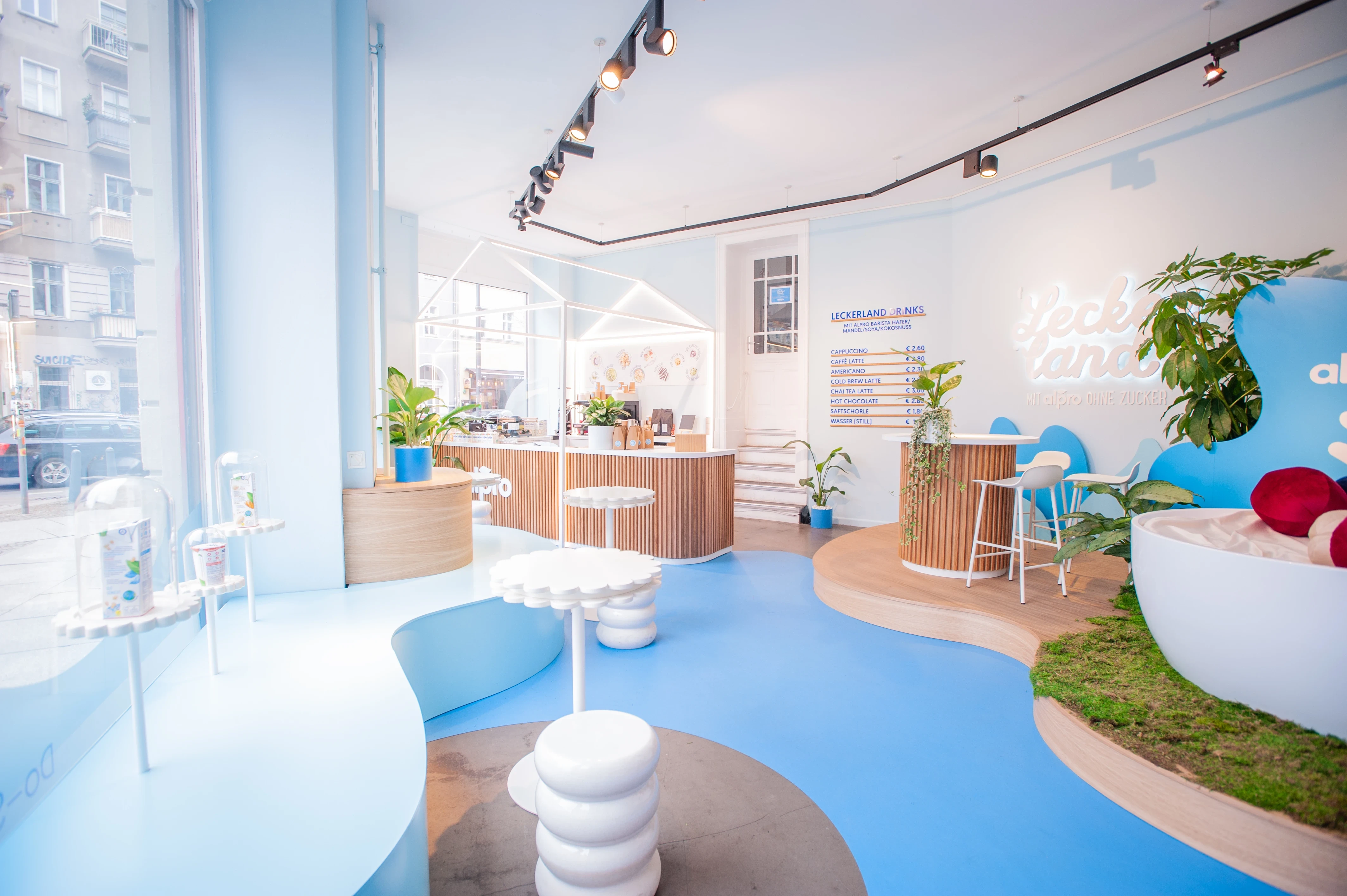 Bright Alpro Leckerland pop-up store with blue floor, flower tables, wooden counters and neon lettering on the wall.