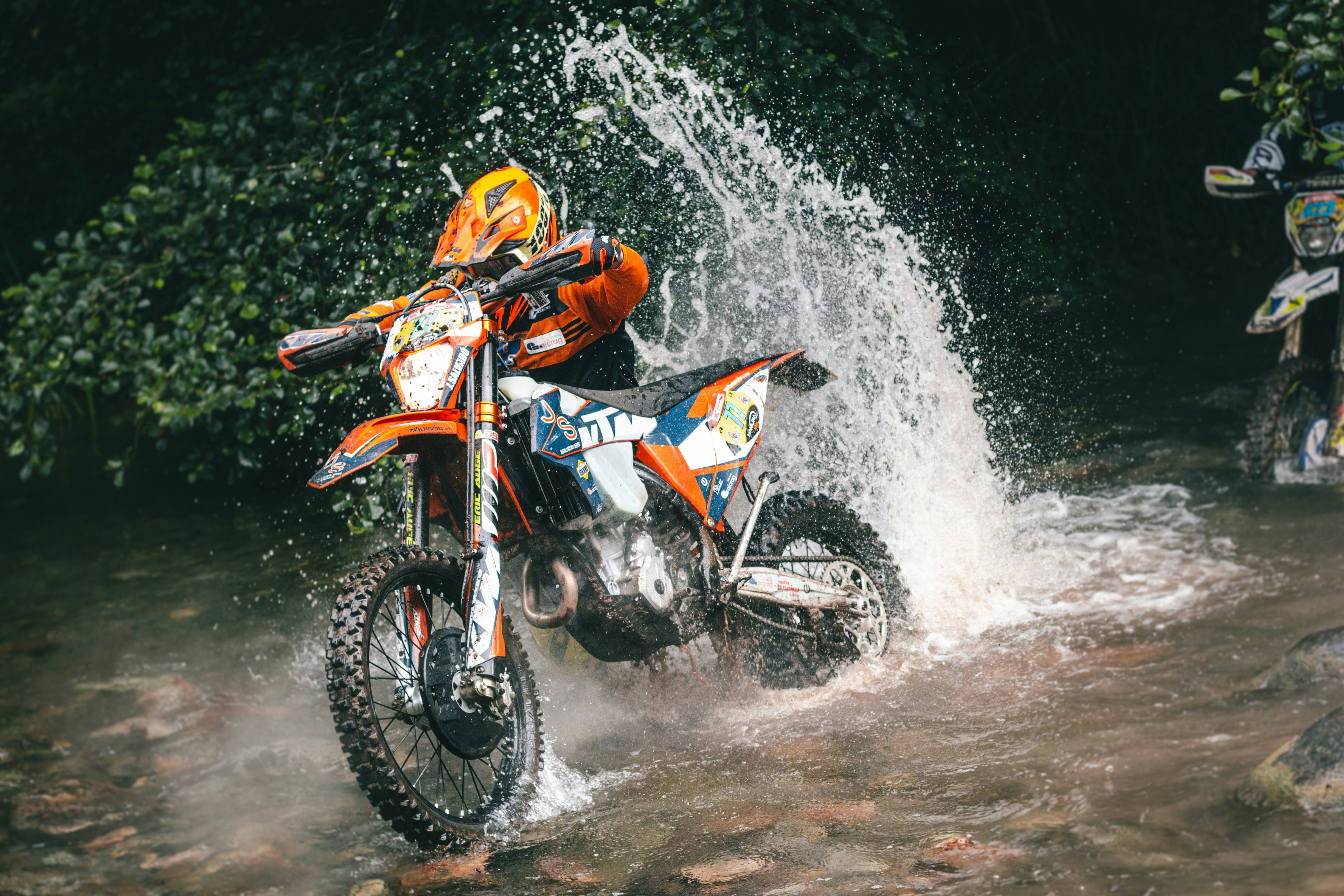 Dirt bike splashes through water near trees