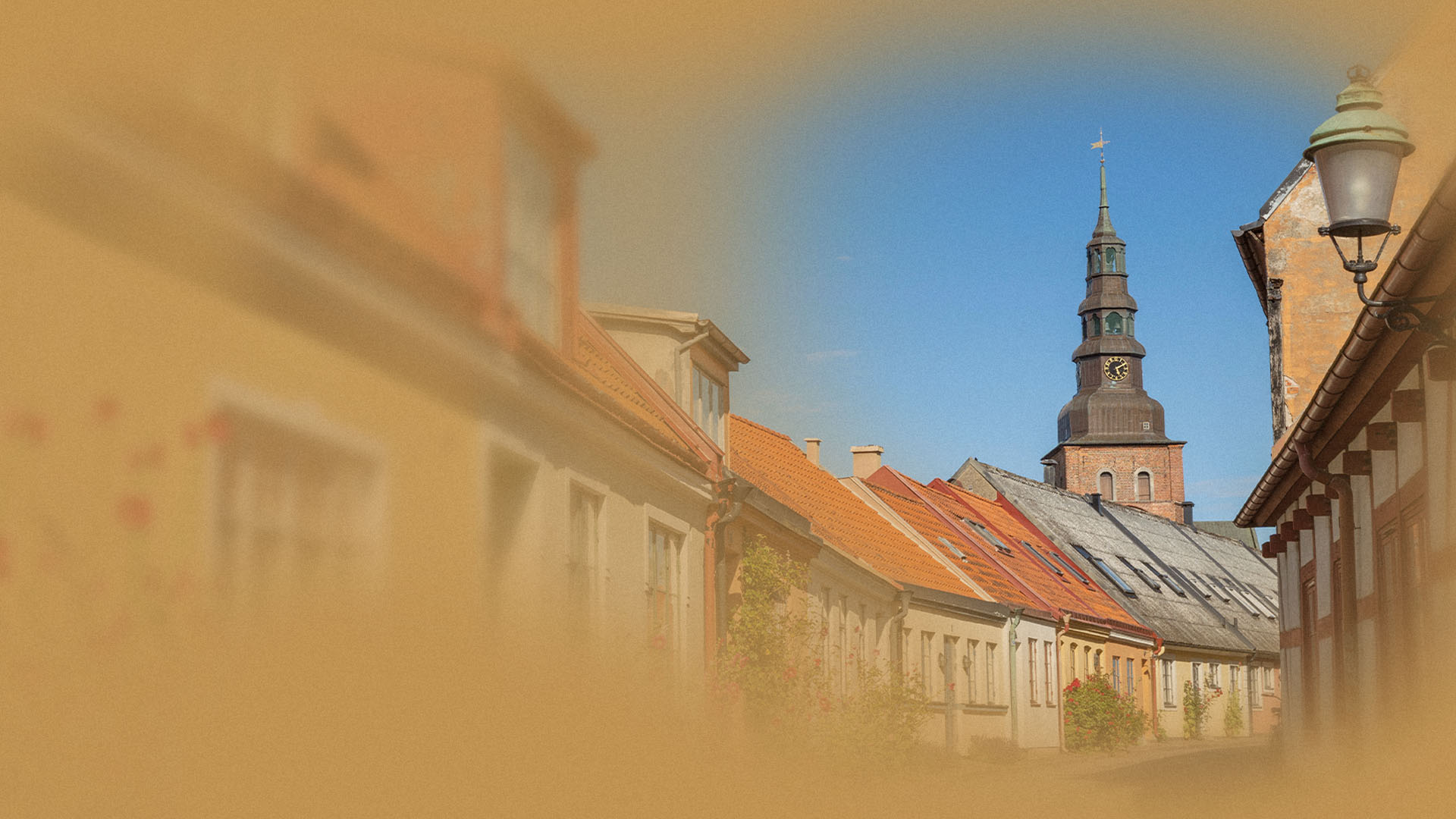 Solig sommardag på Stora Östergatan i centrala Ystad med kyrktornet och gamla gatlyktor