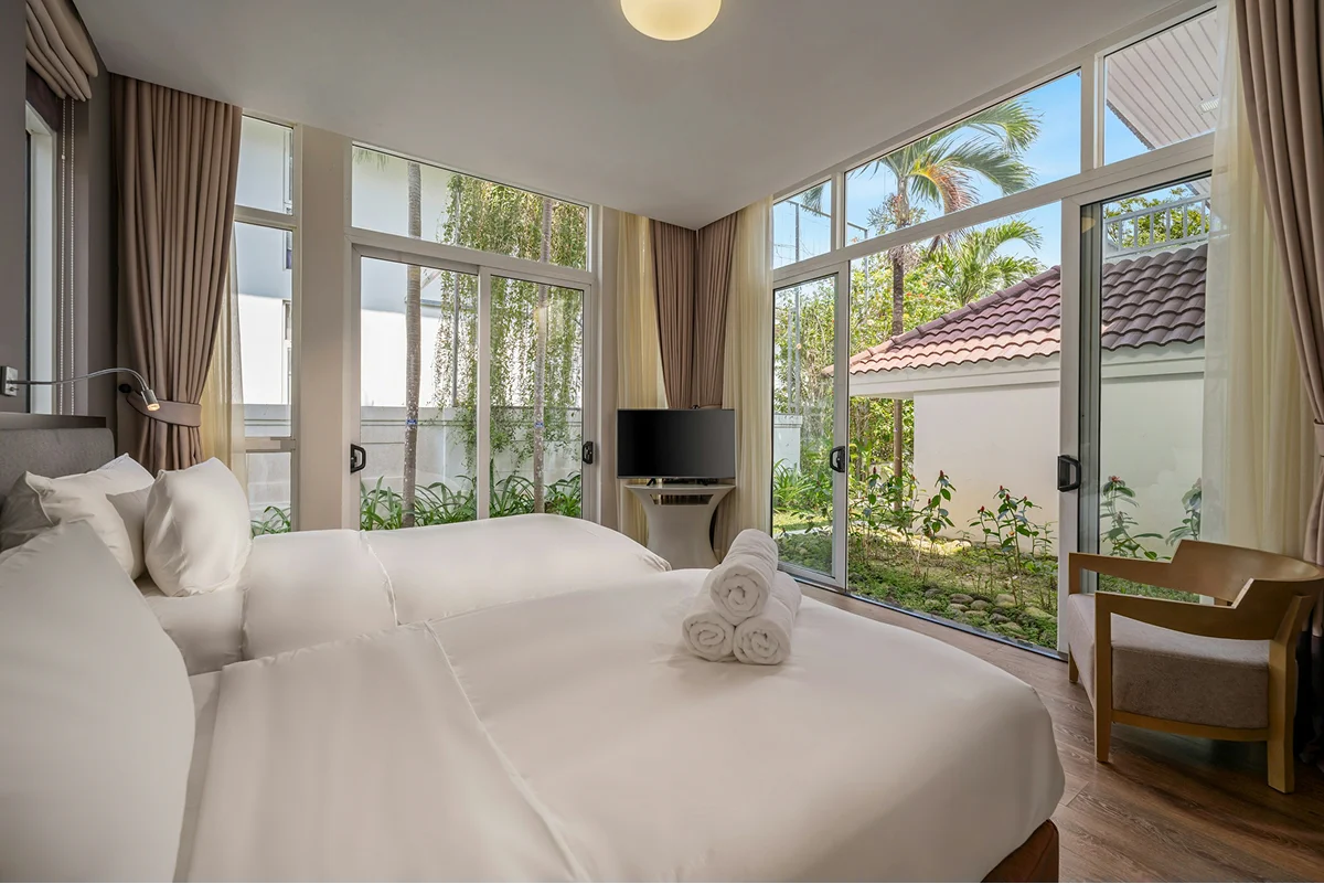 Garden twin room with a large bed, corner windows, and relaxing views of tropical greenery.