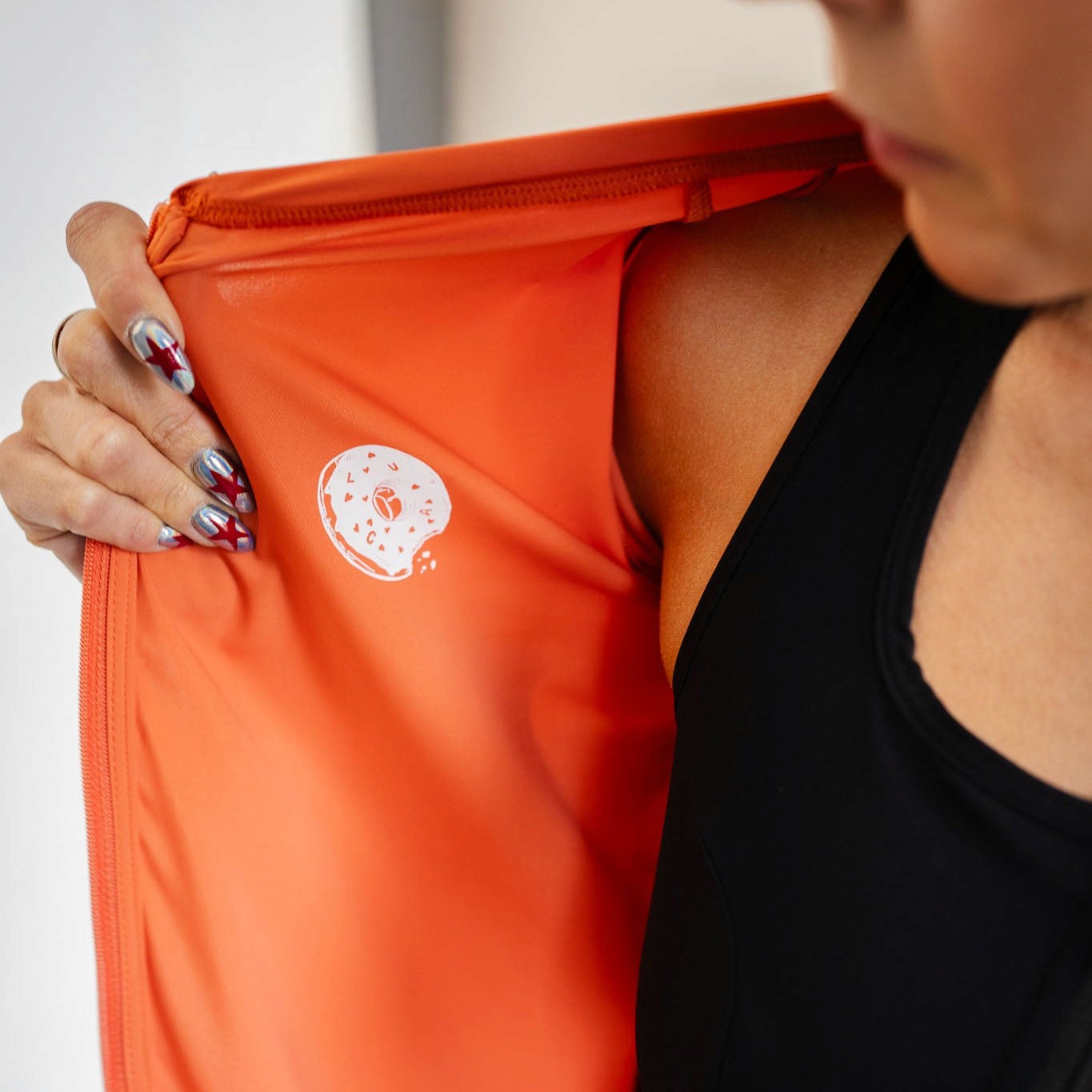 Cyclist lifting LUCA Soleil jersey in aperol to show interior fabric and donut print