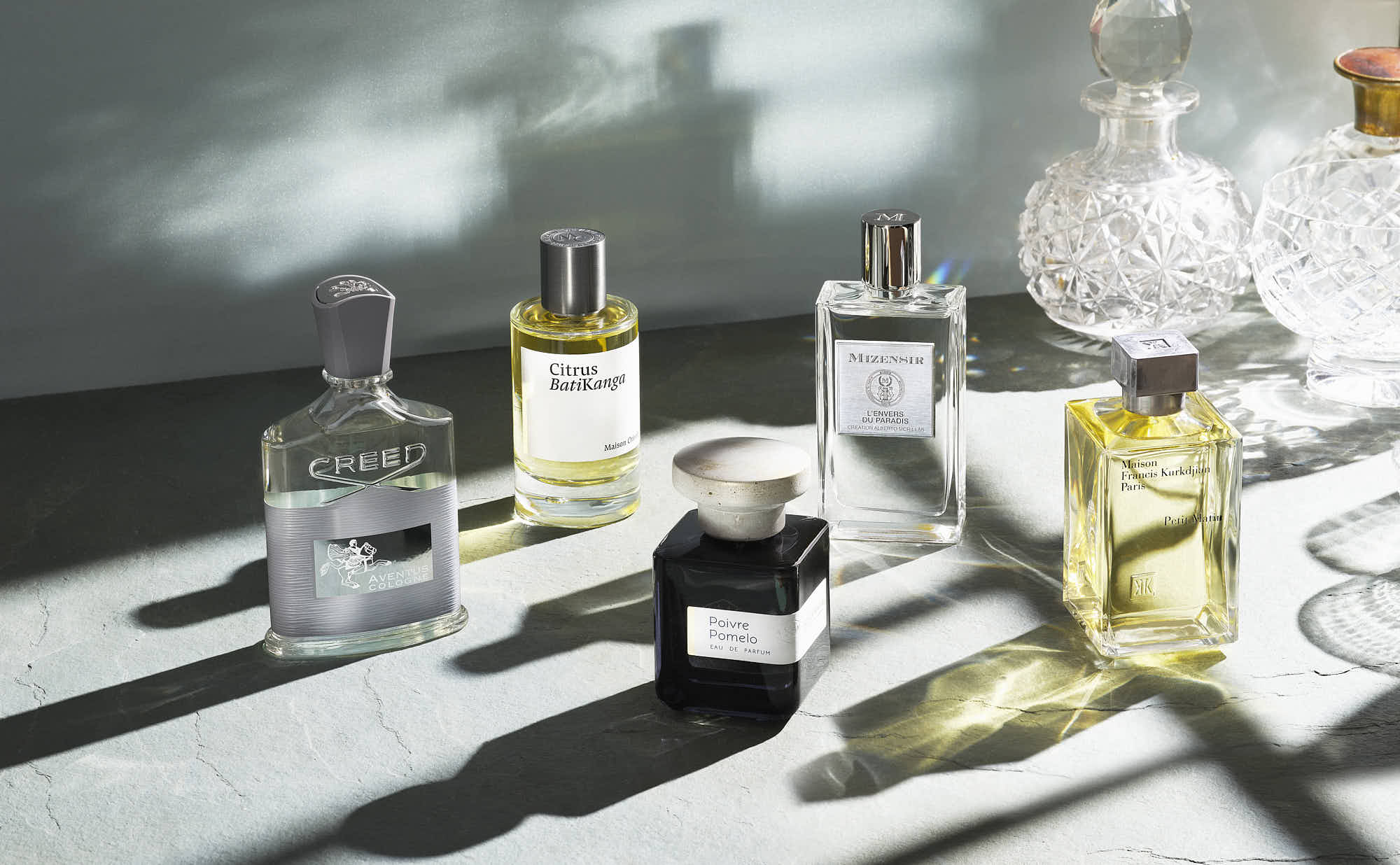 A minimalist arrangement of various perfume bottles on a light surface, with soft shadows and bright highlights.