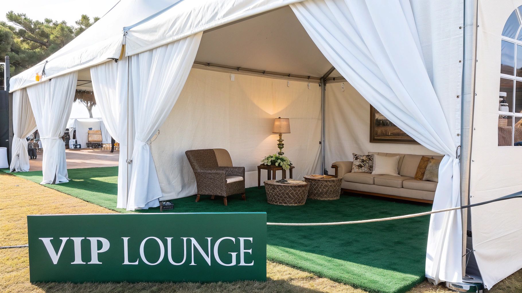 A stylish white tent set up as a VIP lounge with comfortable seating and green turf.