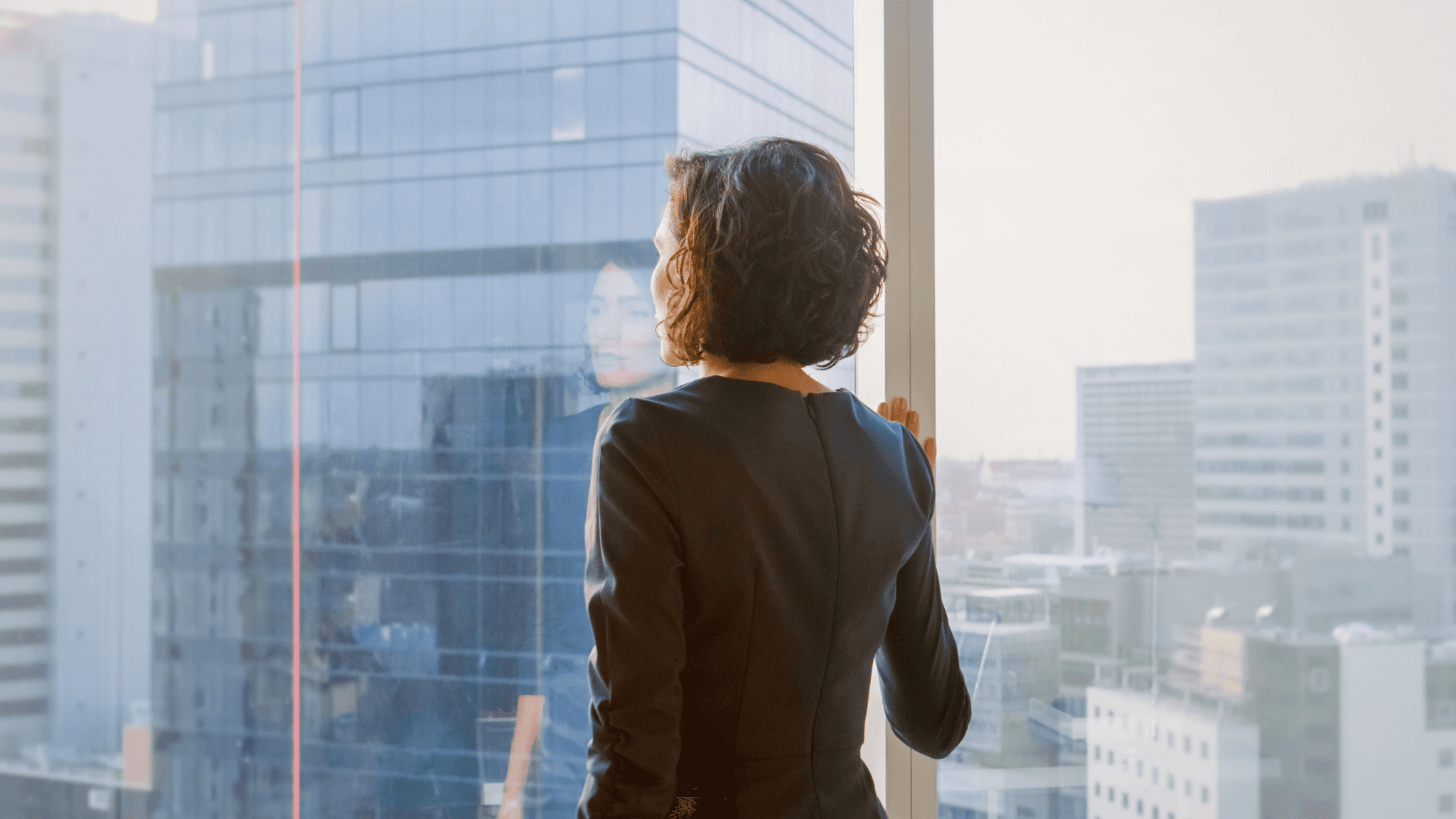 Successful Businesswoman in Her Office Looking out of the Window Thoughtfully. Modern Business Office with Big City View.