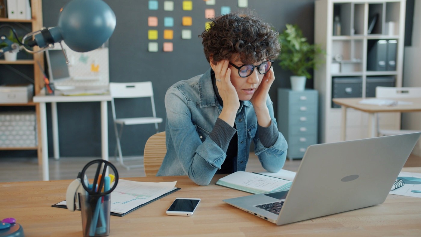 Person stressed at laptop surrounded by manual tasks