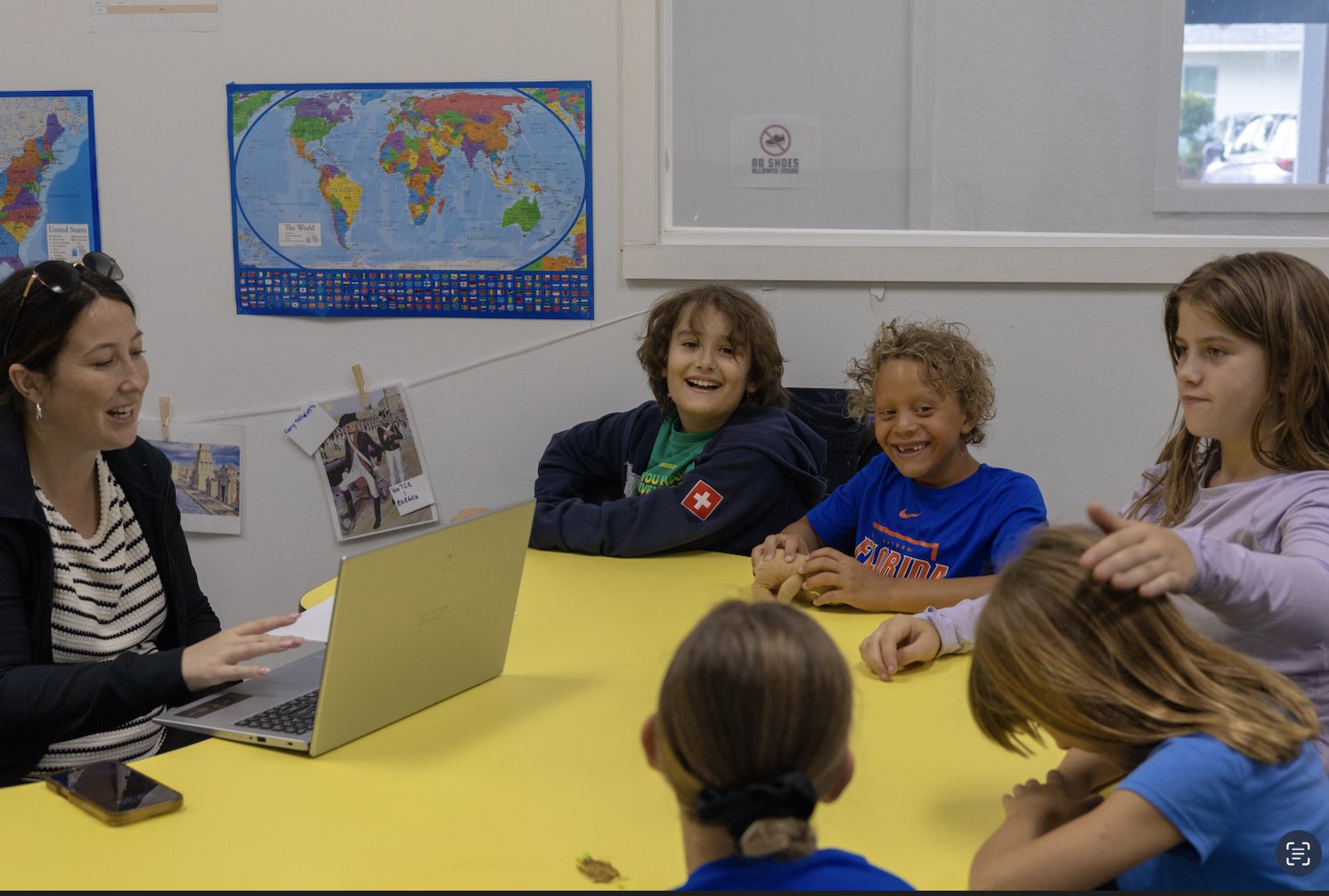 Children and a teacher gathered around classroom activity tables