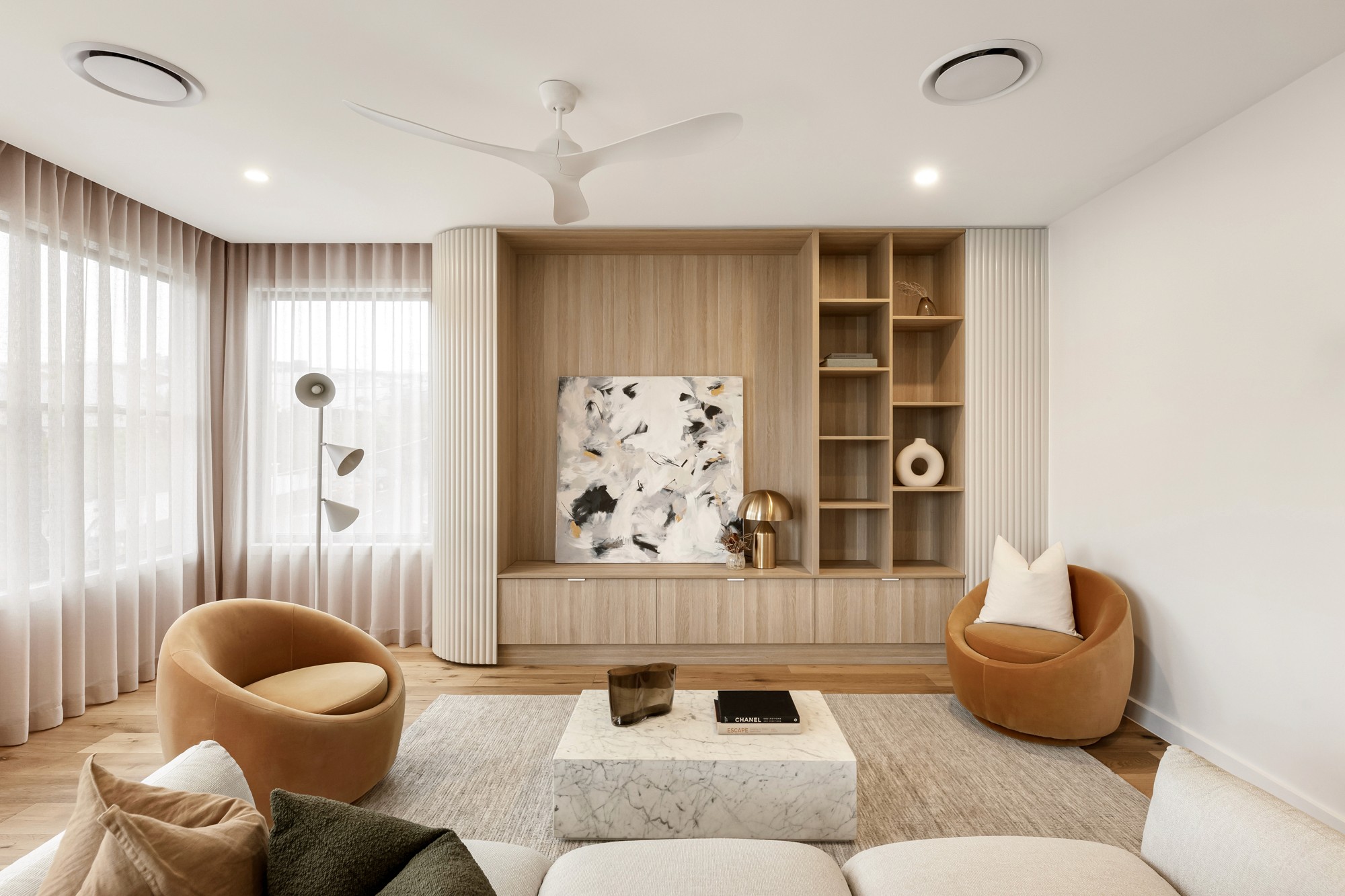Living room featuring light timber joinery, curved furnishings and soft neutral textures.