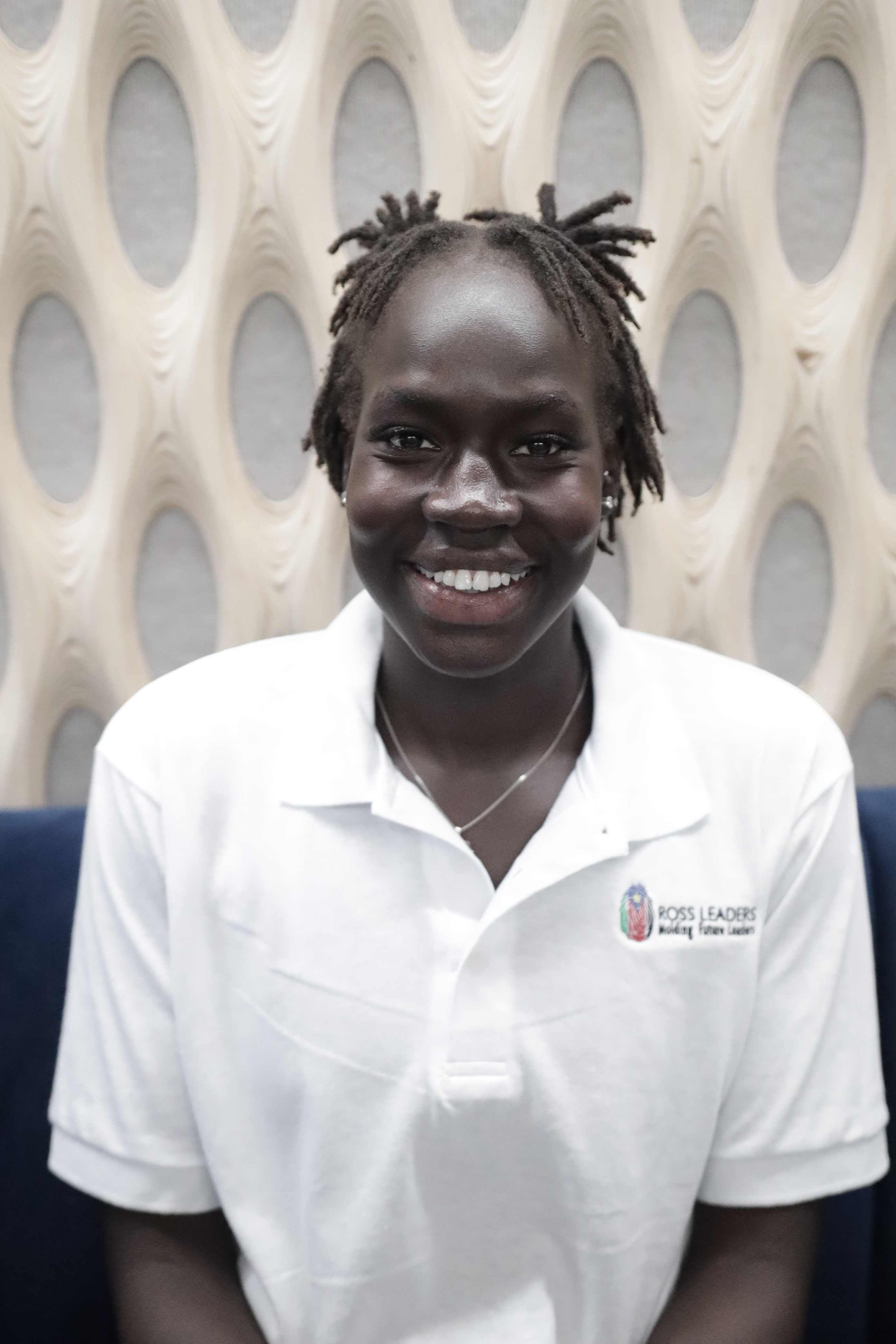 Portrait of a person with red hair, wearing a rust-colored outfit and scarf, set against a neutral gray background.