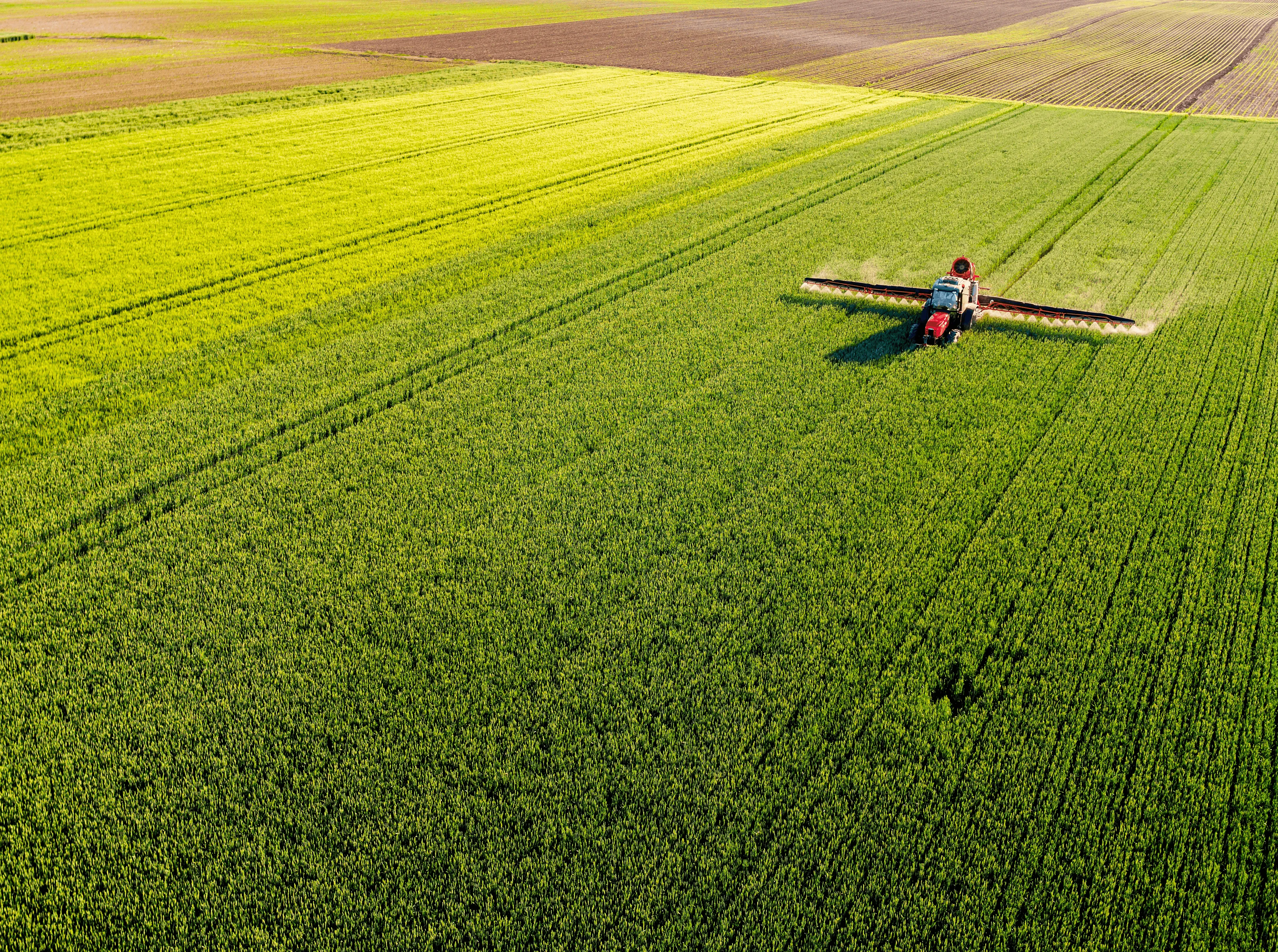 Aerial view of lush green fields, showcasing agricultural land with a tractor working in the distance.