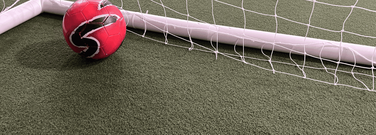 Red soccer ball resting inside a soccer net on a turf grass field