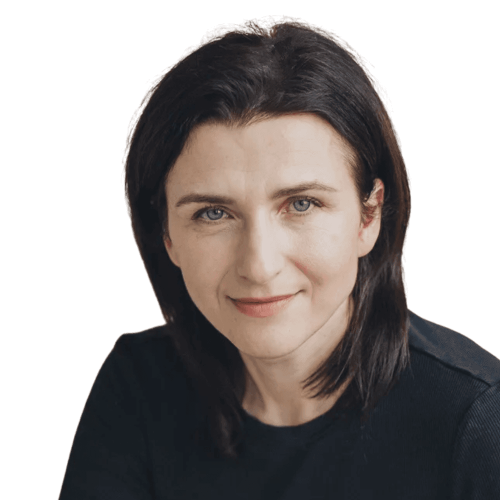 A young person with curly hair smiles at the camera while sitting in front of a laptop against a dark background. (Background Removed)