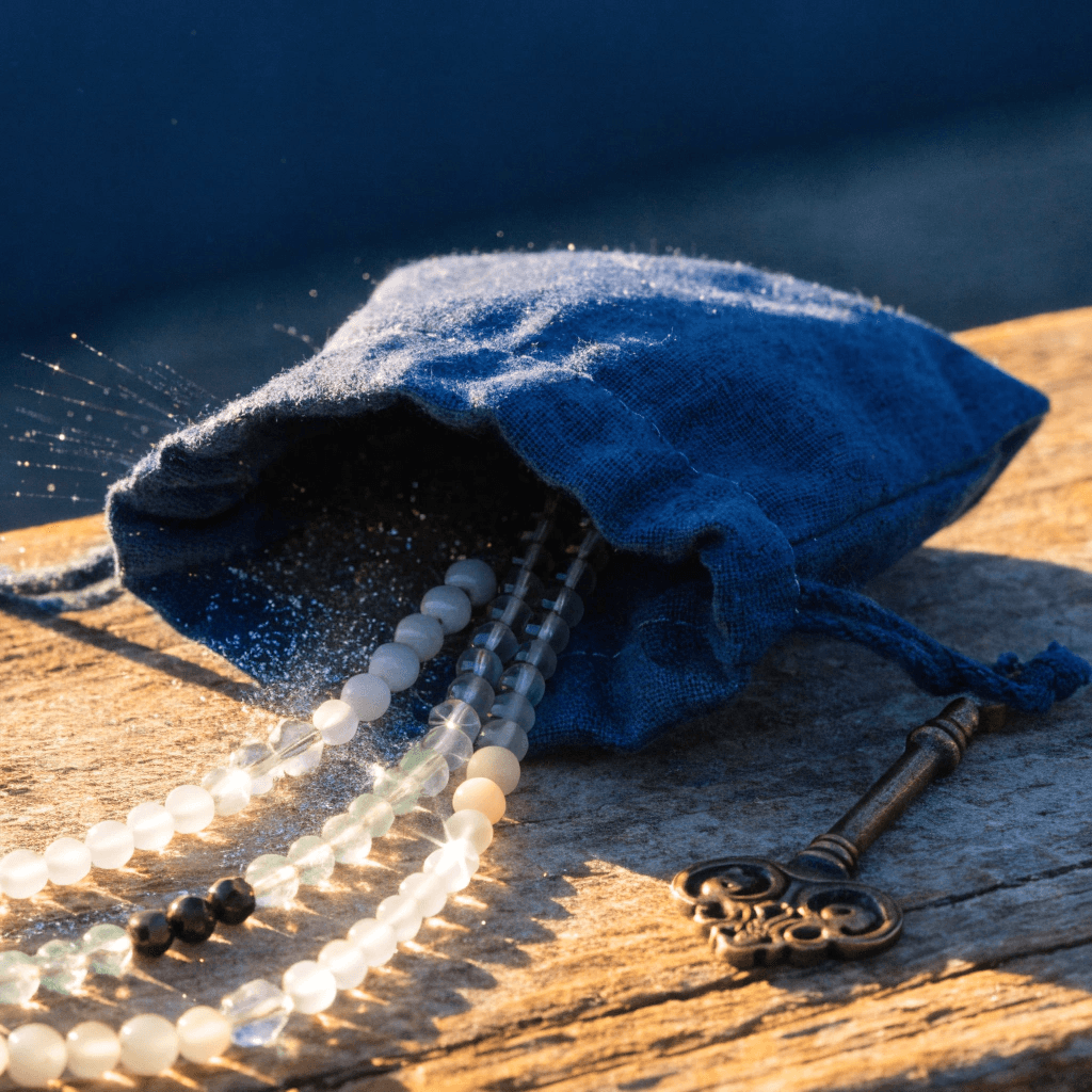 A hyper-realistic macro photograph of a rustic wooden surface during a warm golden hour sunset. Resting on the wood is a small drawstring pouch made of textured #2E345E Celestial Indigo canvas, spilling out delicate, glittering silver dust and a few handmade beaded spiritual bracelets.