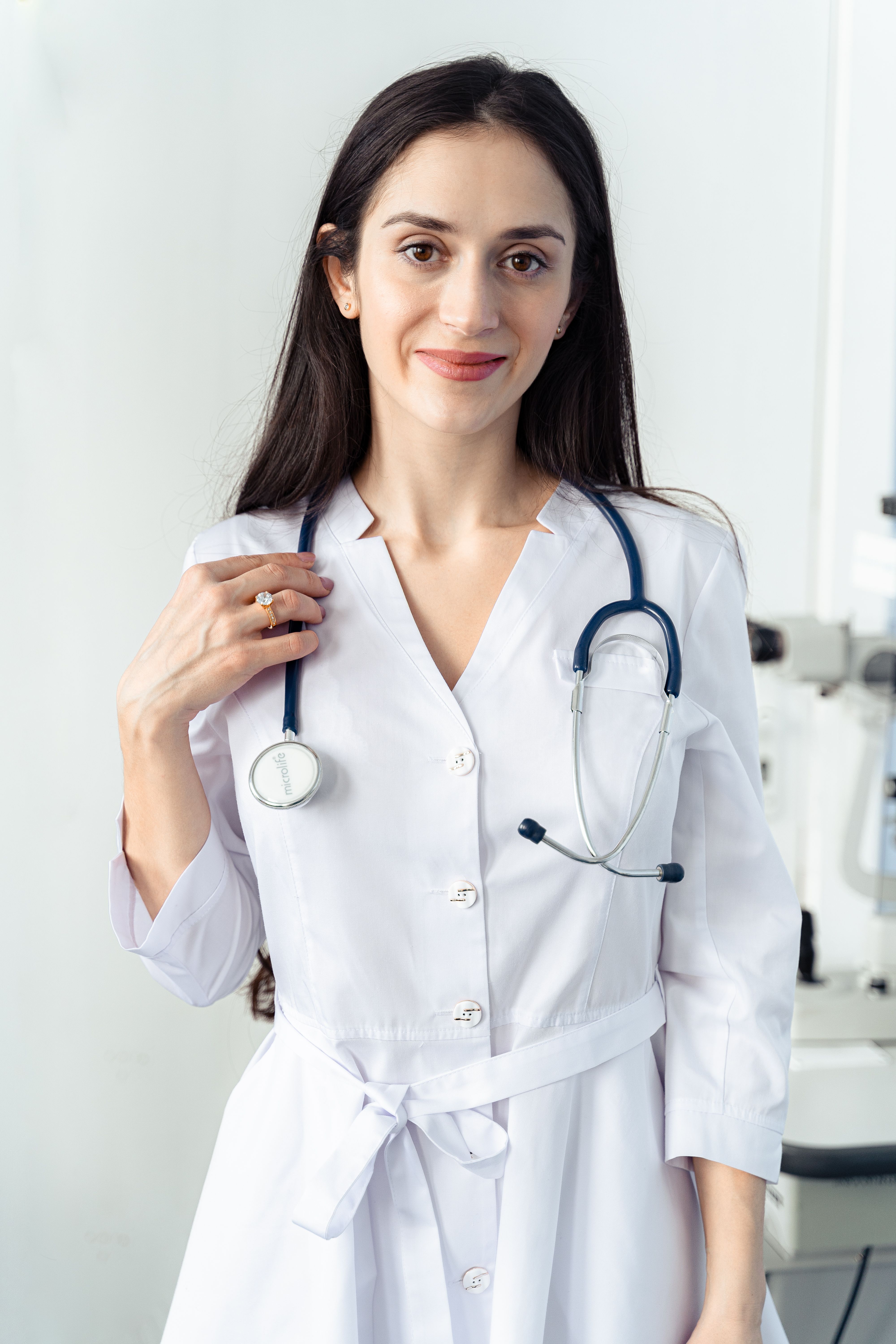 A woman with dark curly hair wearing teal medical scrubs with arms crossed