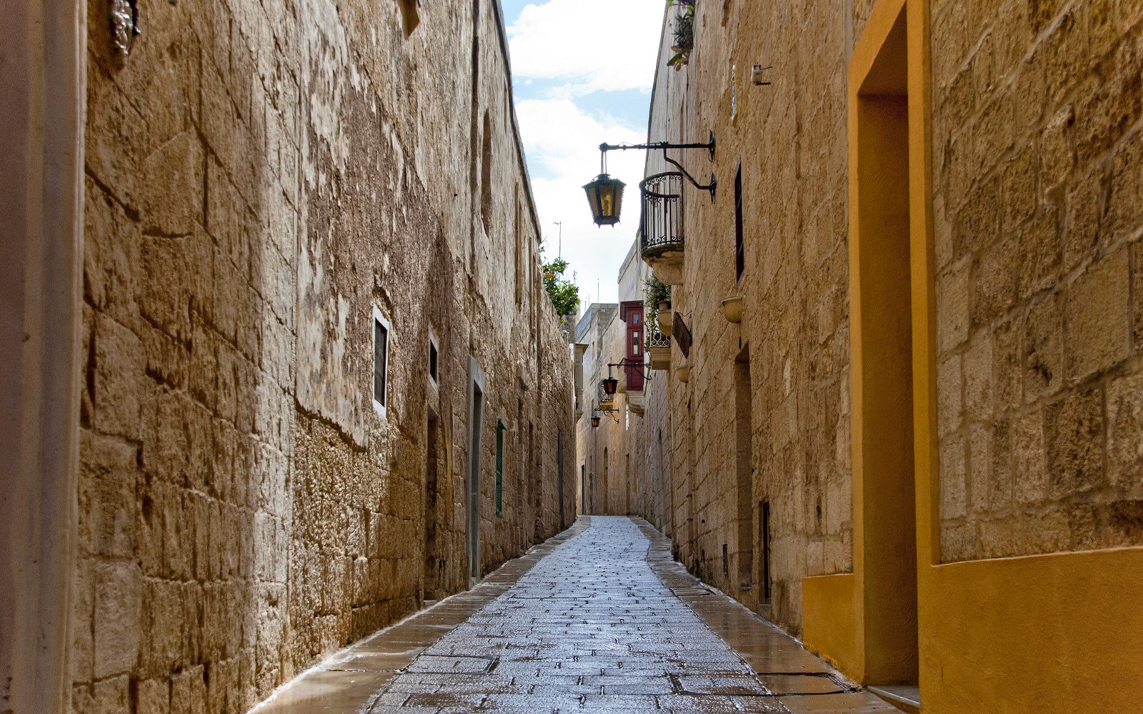 Narrow cobblestone street in Mdina, Malta, lined with historic stone buildings.