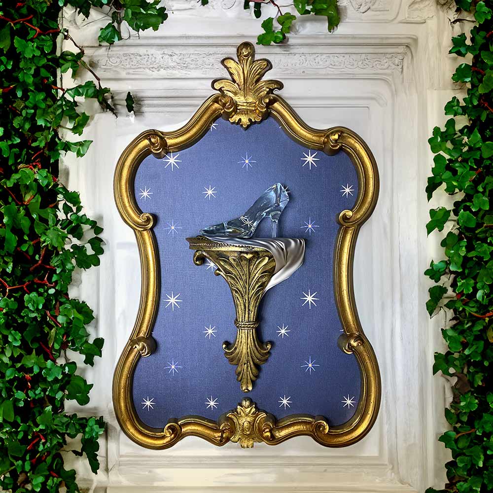Image of a gilded frame with star night wall paper backing with a mounted wall shelf holding a glass slipper