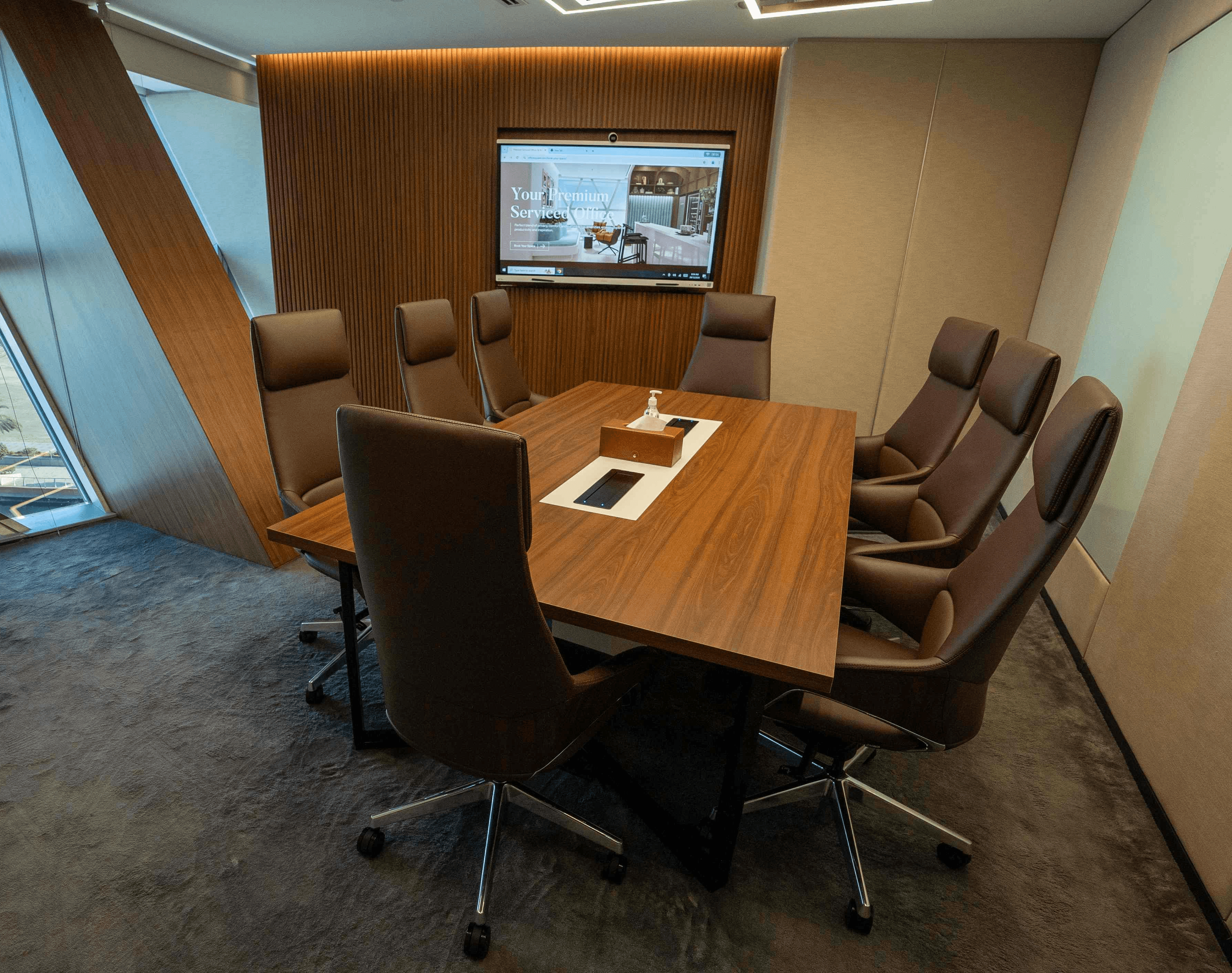 Premium meeting room in Abu Dhabi featuring a wood-paneled wall, high-definition screen, and an 8-seater conference table.