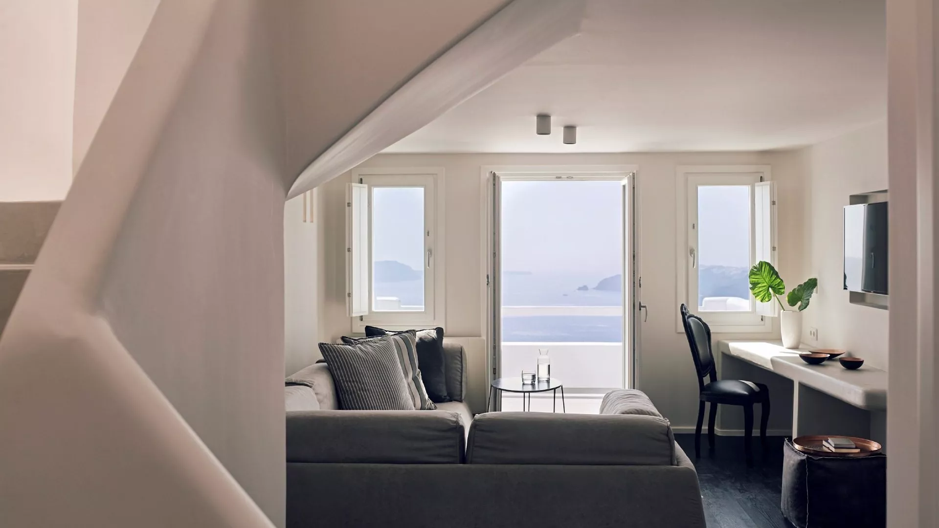 Helles Wohnzimmer mit Sofa, Schreibtisch und Meerblick durch große Fenster.