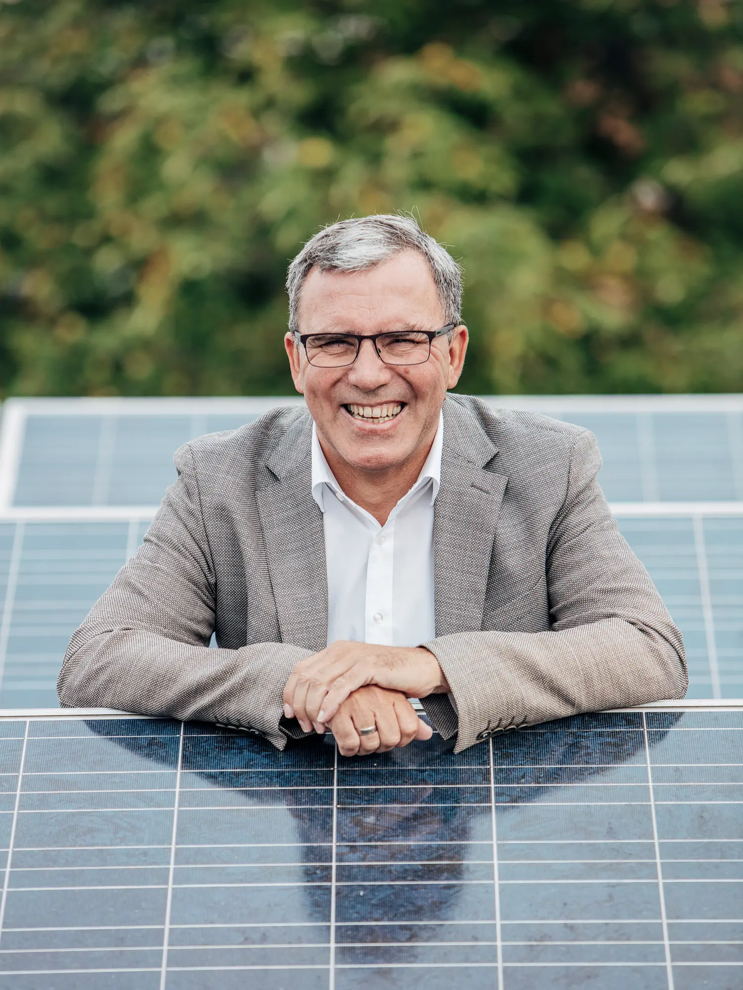 Lächelnder Mann mit Brille lehnt an Solarpanel im Freien