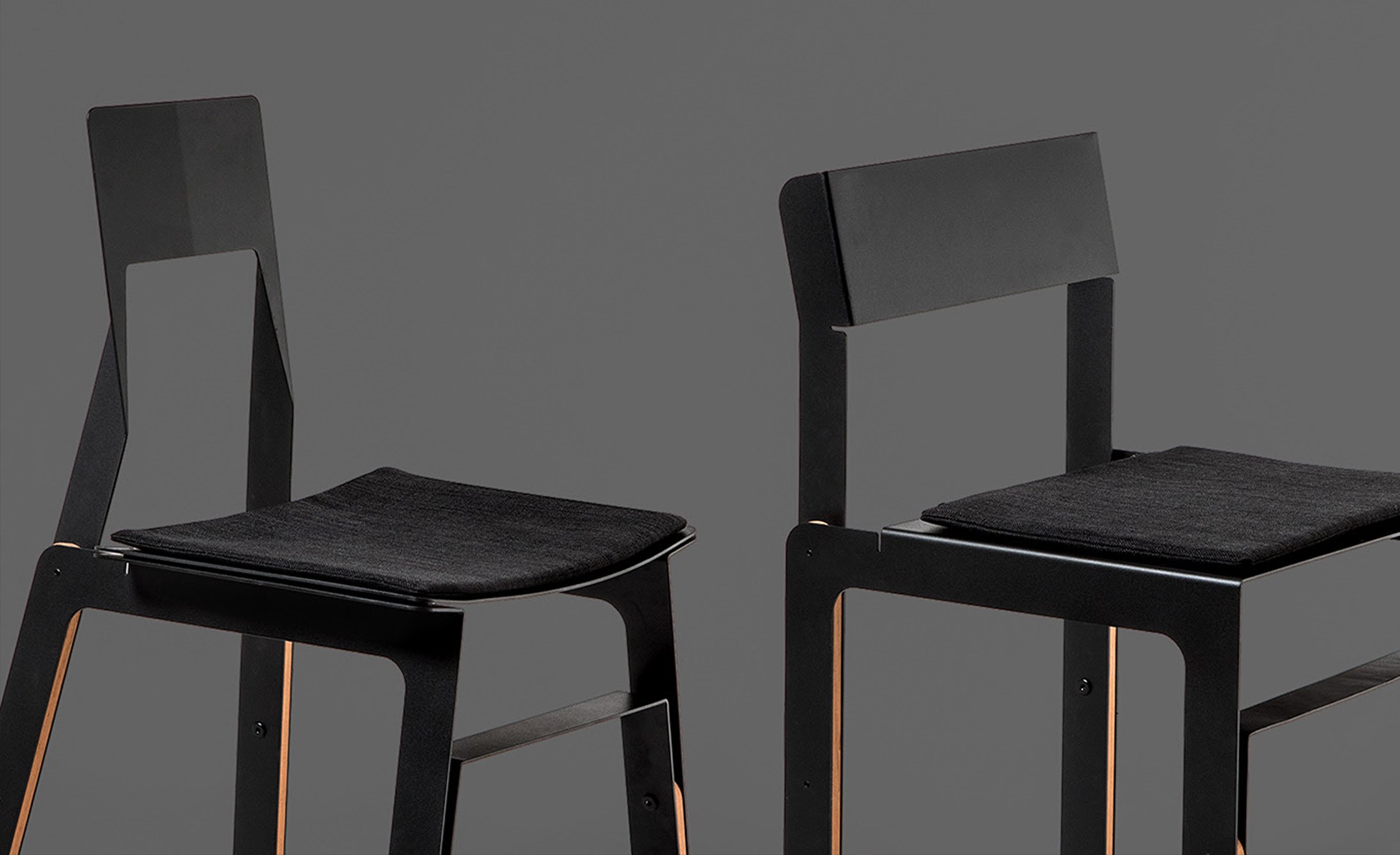 Two modern black chairs with simple designs, one with a cutout in the backrest, and both featuring black cushioned seats.