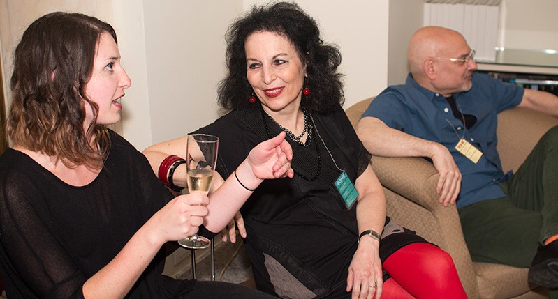 two women talking holding a champagne glass and a man on the back