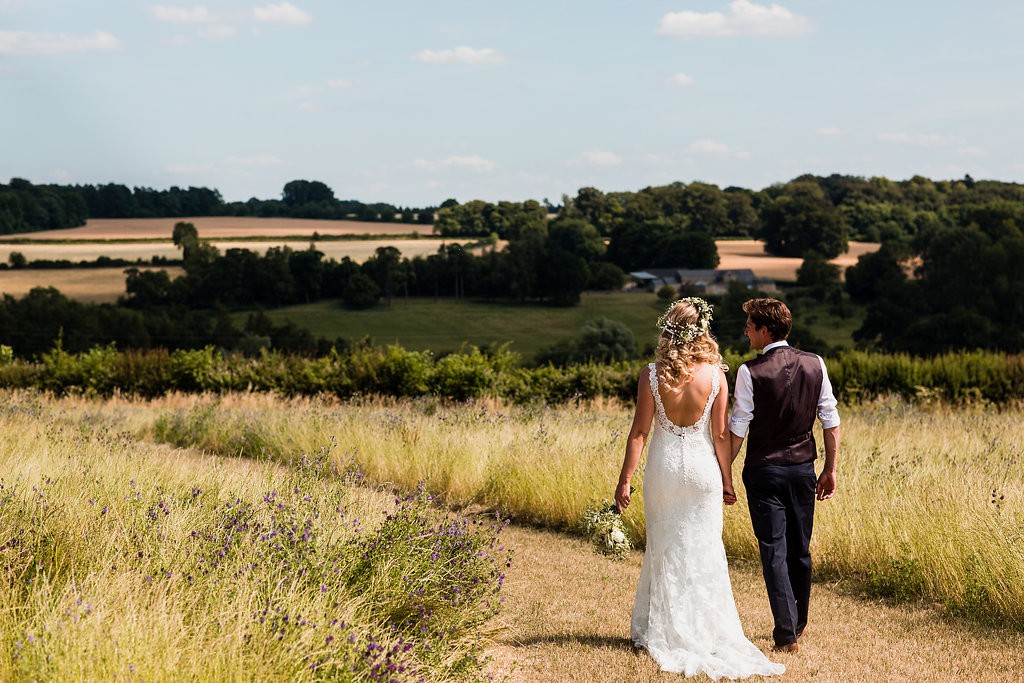 A newlywed couple walking through the meadow overlooking the Cotswold countryside.