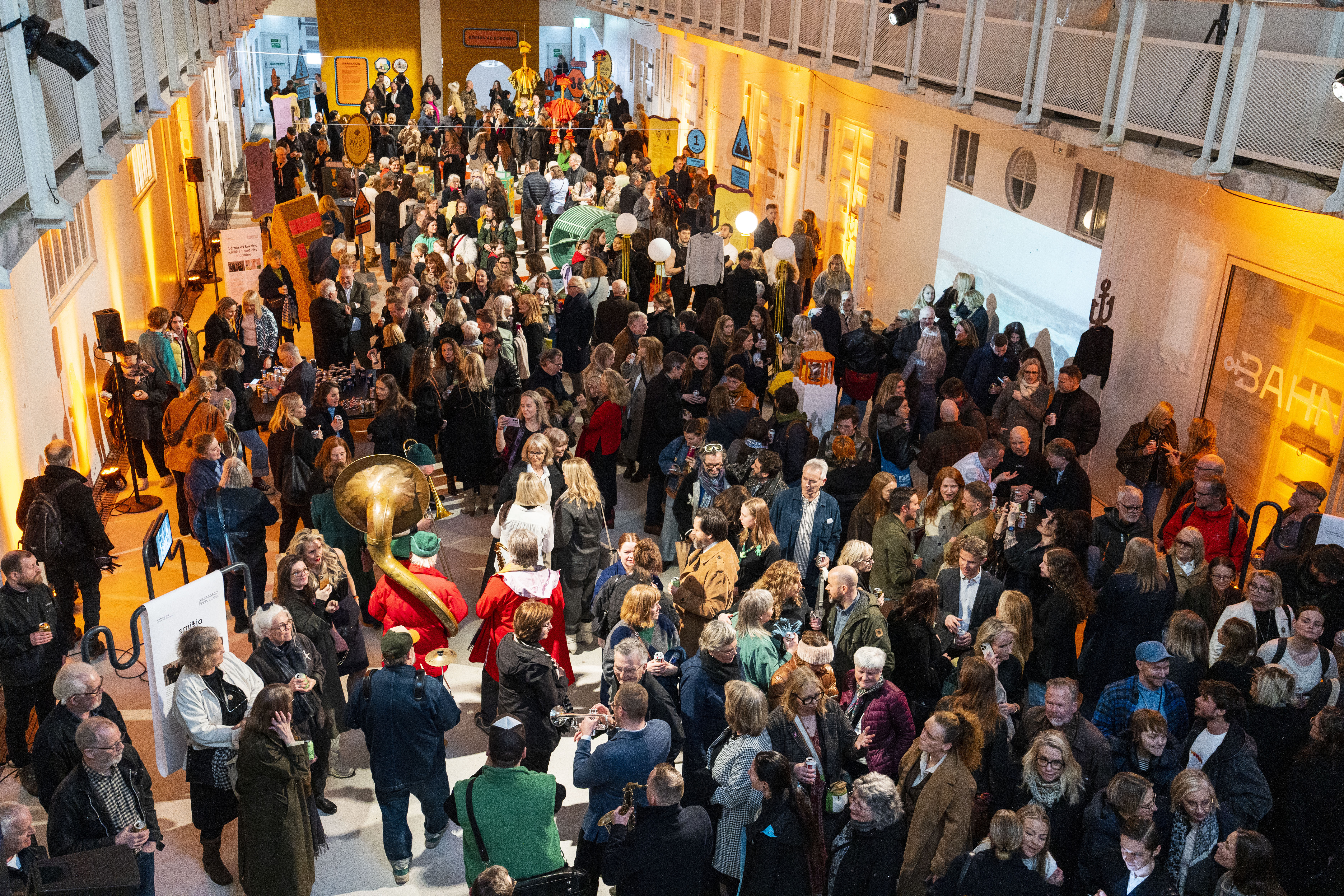 A crowded indoor hall during DesignMarch opening night with warm lighting, many attendees, and a musician in the foreground. Photo: Miðstöð hönnunar og arkitektúrs