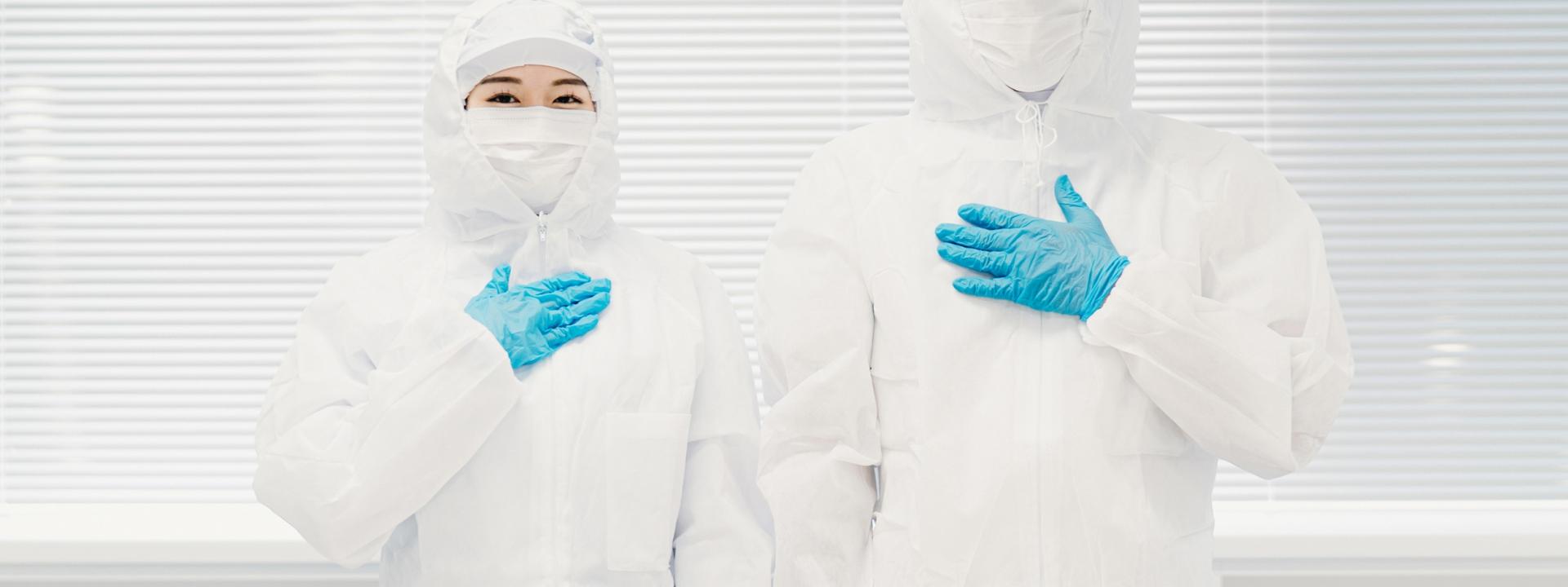 胸に手を当てる防護服の2人