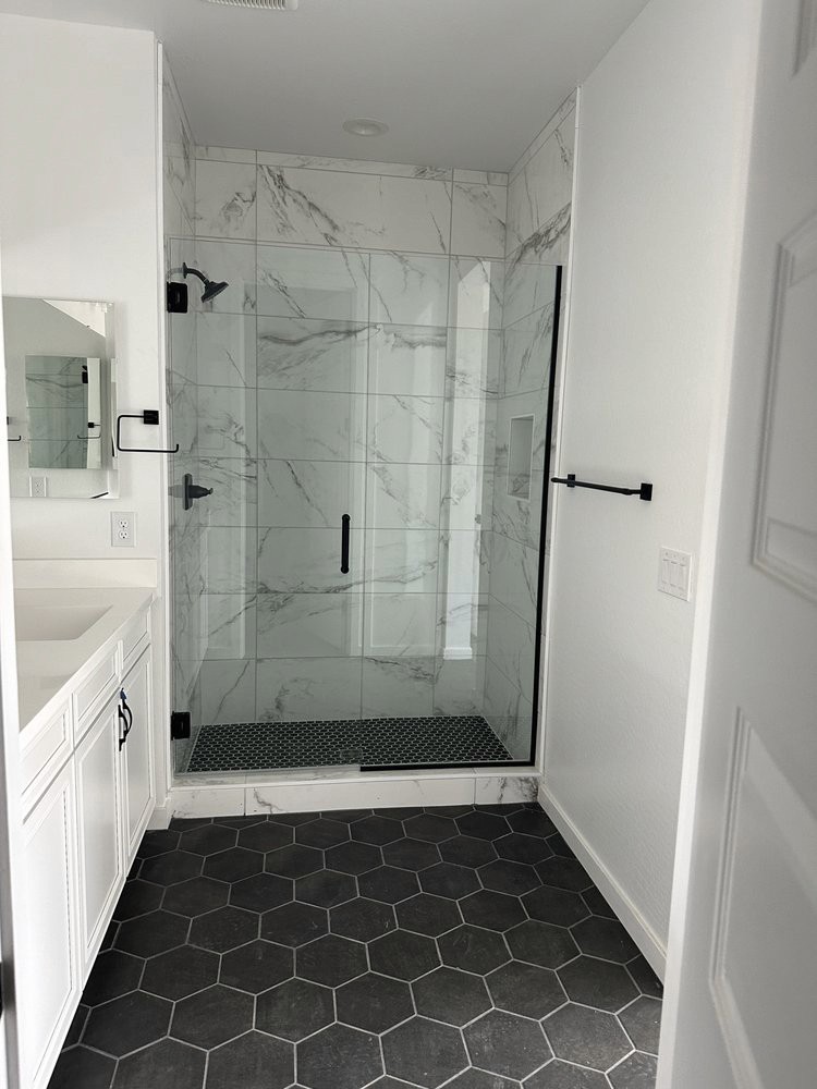 Contemporary bathroom featuring a large walk-in shower with white marble-look wall tiles and a black and white patterned mosaic shower floor, complemented by black hexagonal floor tiles throughout the bathroom.