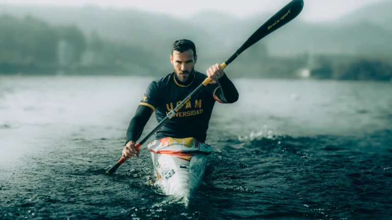 A focused athlete paddles powerfully in a sleek kayak on a misty lake, embodying the disciplined spirit associated with training in a European master in high performance sports program.