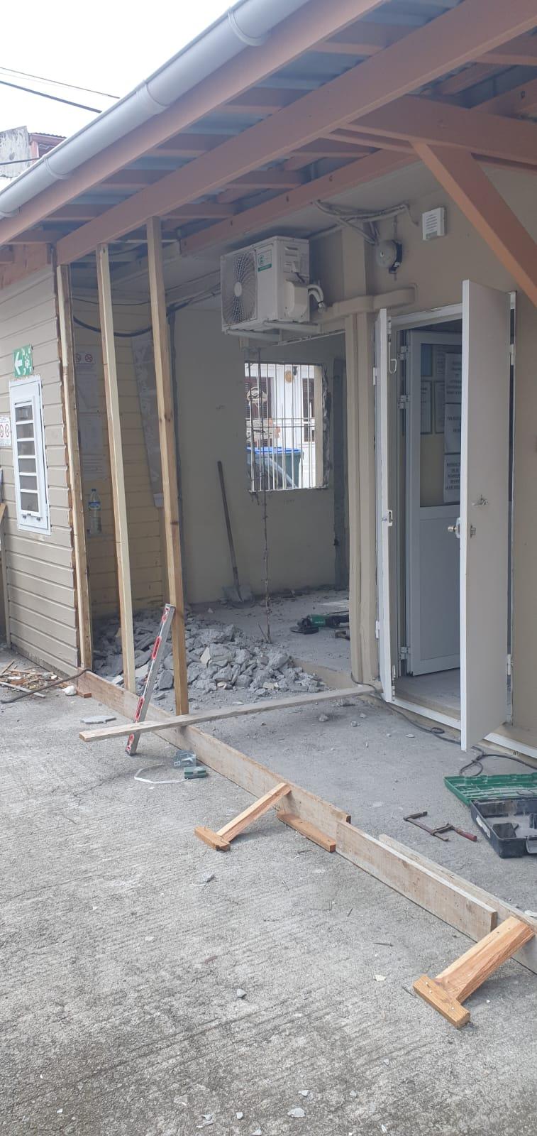 Bâtiment en rénovation avec un mur ouvert laissant apparaître la charpente et des débris. Une porte est ouverte et des outils de construction sont éparpillés, donnant l'impression que les travaux sont en cours par Agenov en Martinique.