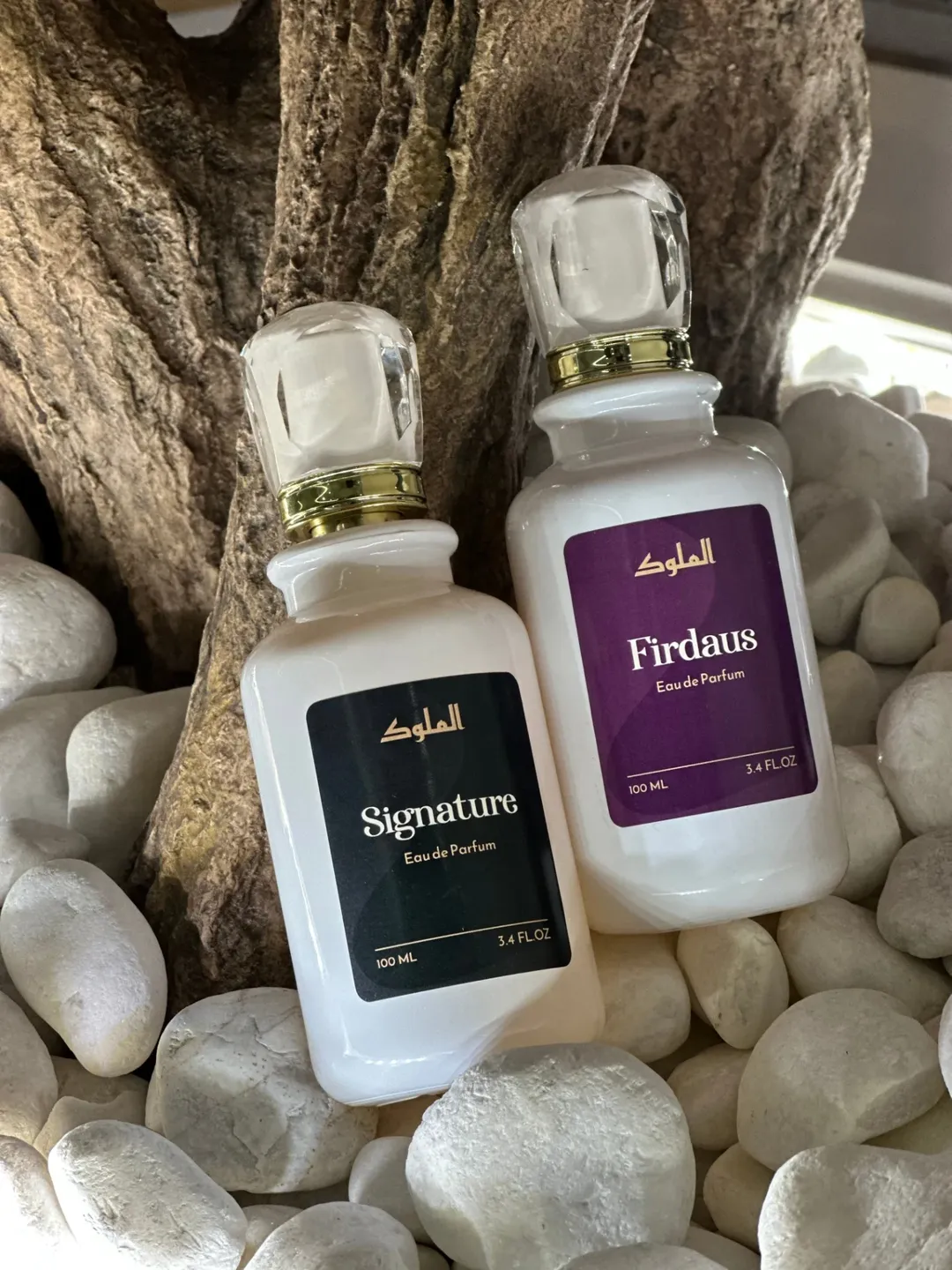 Firdaus purple perfume box and Signature bottle styled on textured white stones.
