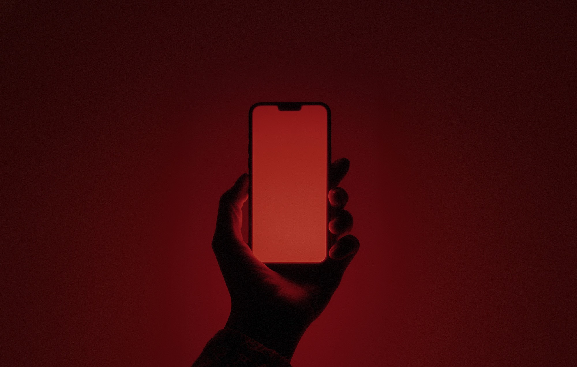 Hand silhouette holding a smartphone with a glowing red screen.