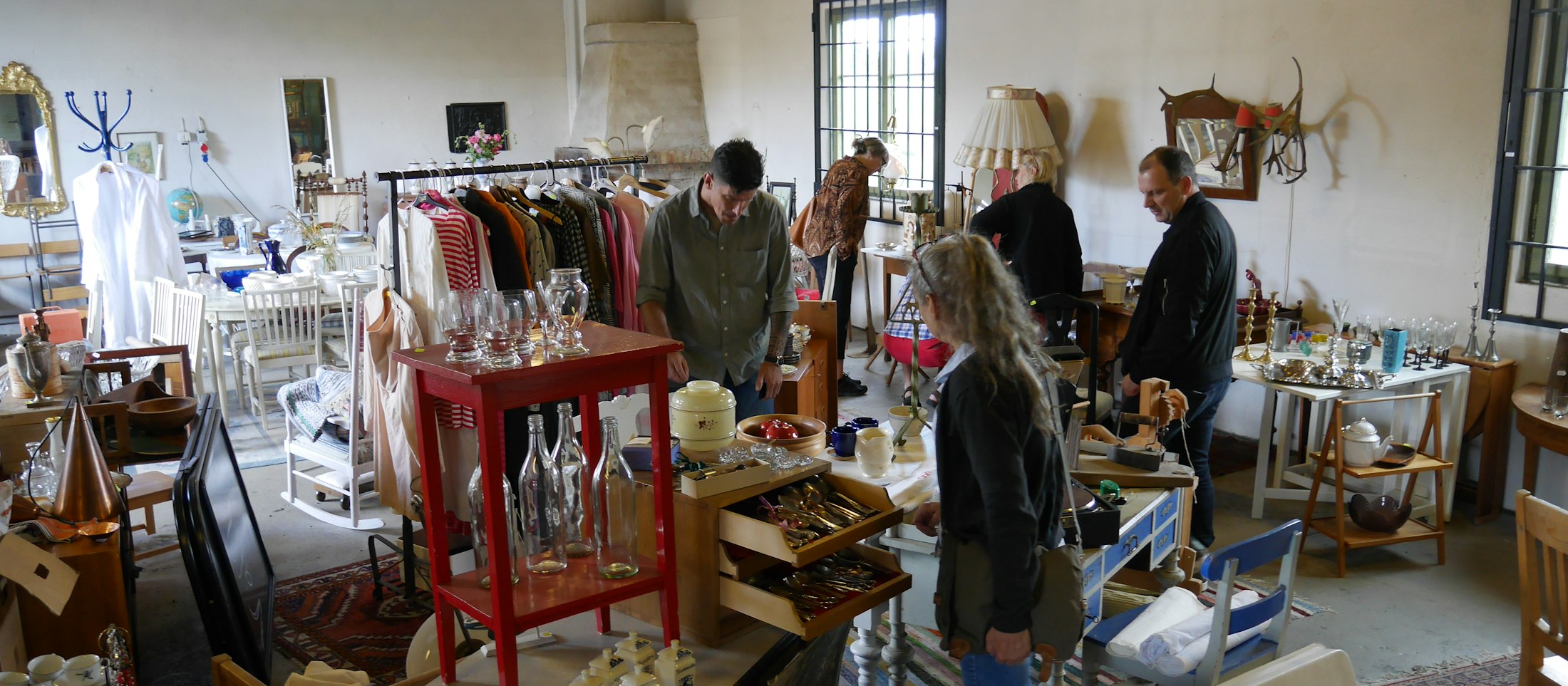 People browsing furniture and clothing racks in a market hall