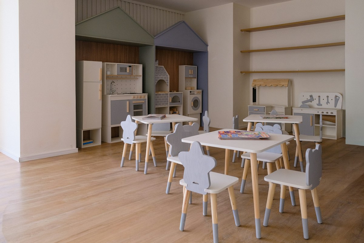 A bright nursery room with small tables, star-backed chairs and a play kitchen