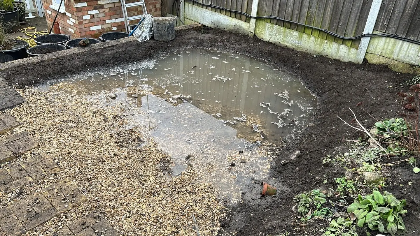 An unfinished garden area with a curved outline, showing soil, gravel, and some greenery around the edges.