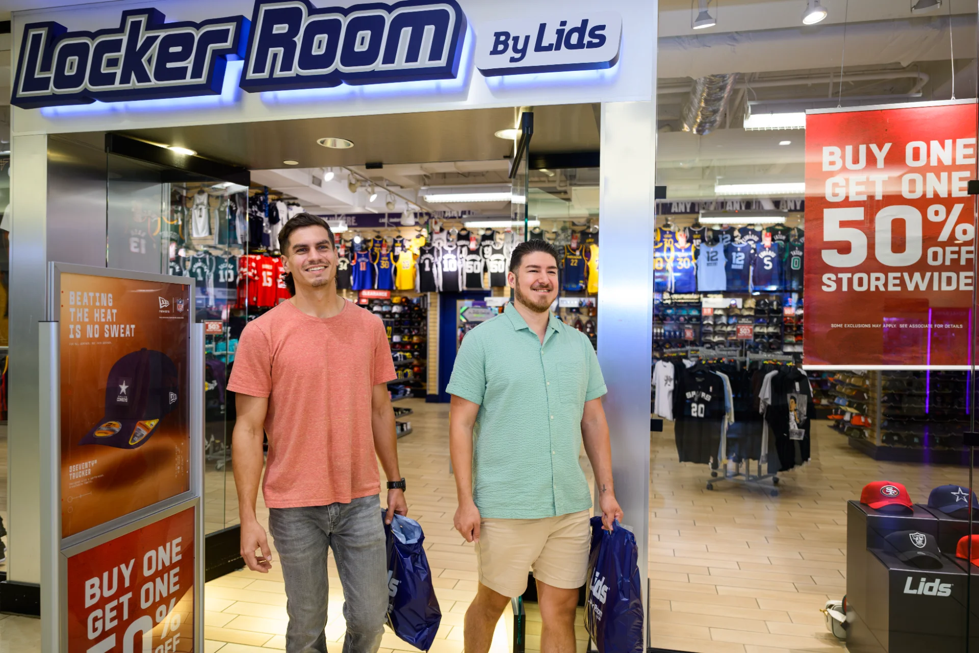 Two shoppers leaving Locker Room by Lids with team merchandise bags under a buy-one-get-one sign
