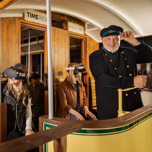 Seorang konduktor dan tiga orang yang memakai headset VR berada di dalam trem kayu bersejarah dengan tanda "Köln 1926".