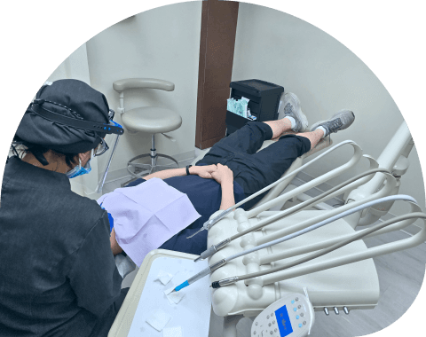 A dental professional wearing protective gear performing a dental procedure on a patient lying in a dental chair.