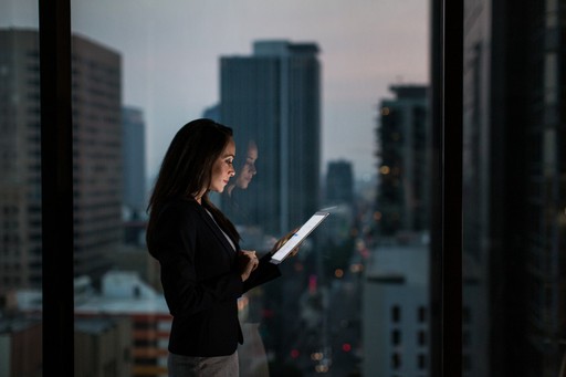 A silhouette of a person standing near a window, reading on a device, with city skyscrapers in the background.