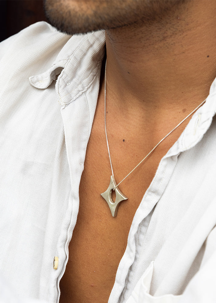 Silver necklace with a star-shaped pendant worn by a person in a white shirt.