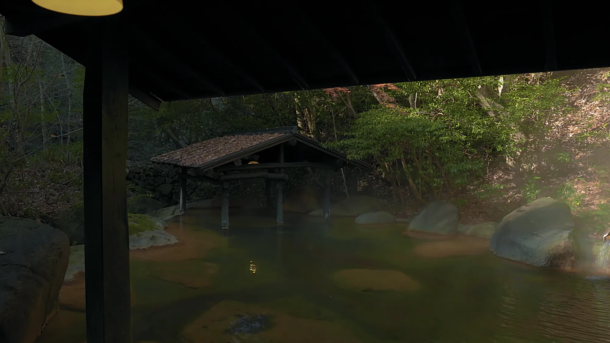 An open-air bath at night under a timber shelter, forest beyond