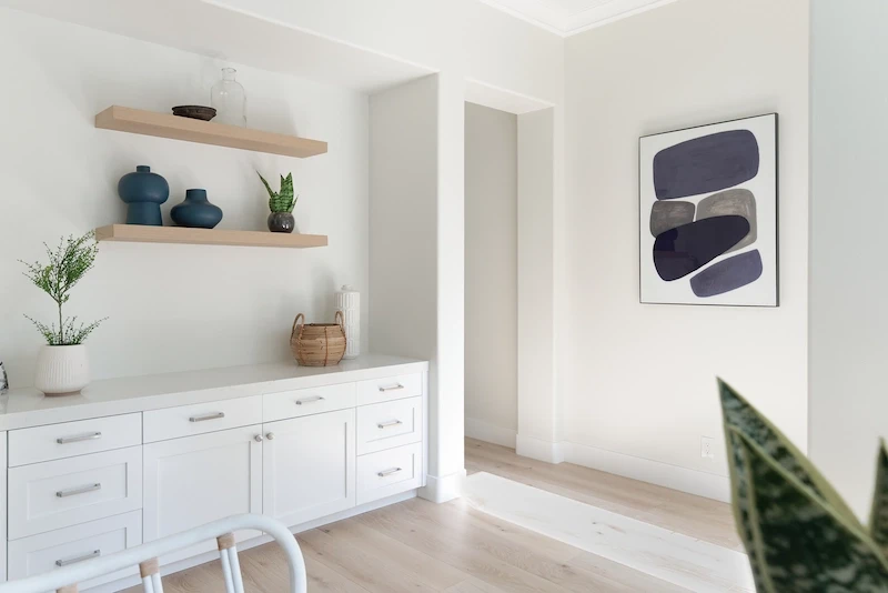 Minimalist dining nook with white built-in cabinets, floating shelves, and modern art in Bonita Canyon Remodel.