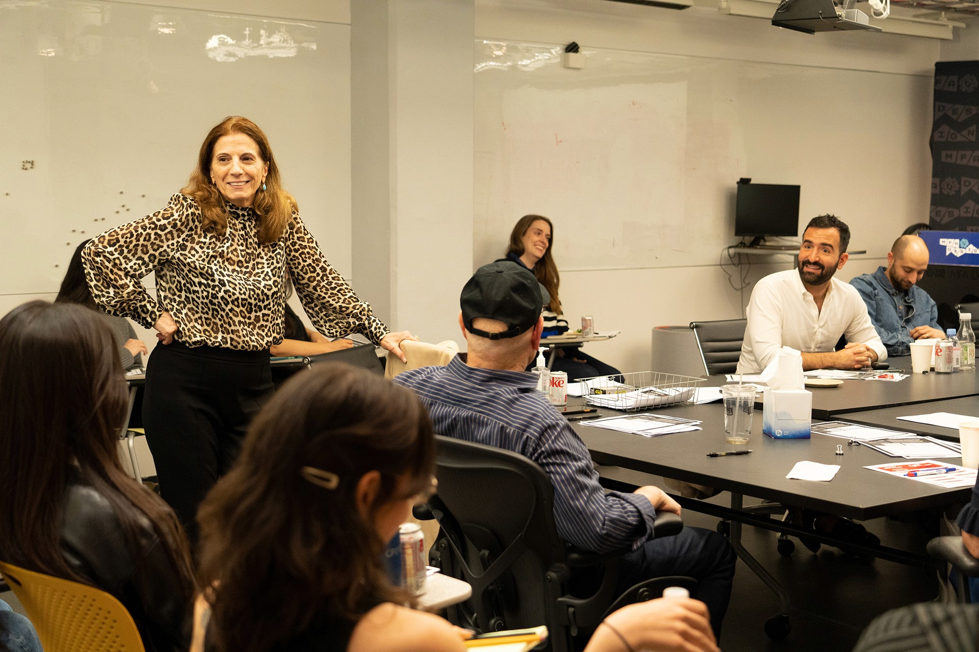 a woman in a animal print blouse smiling to a group of people in a meeting