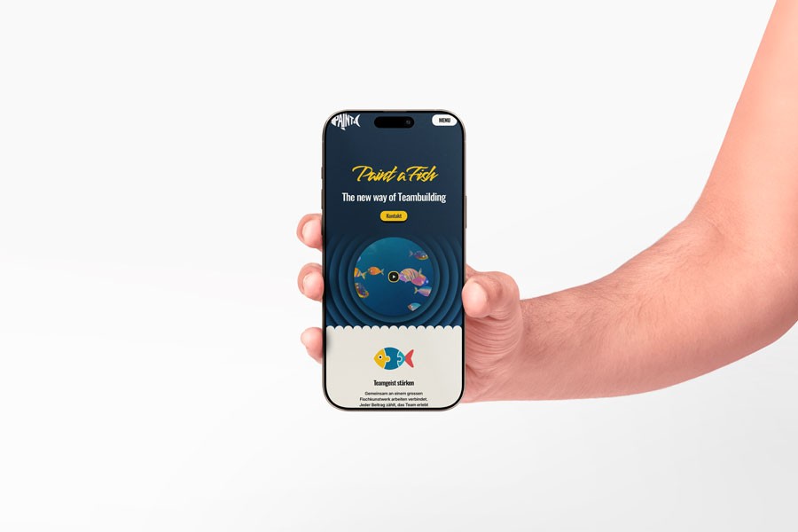Mockup eines iPhones in einer Hand mit geöffneter Paint a Fish Website. Auf dem Display sind das Logo, der Claim ‚The new way of Teambuilding‘ sowie bunte Fische als Designelement sichtbar.